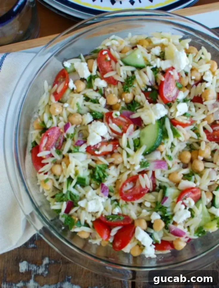 A bright and fresh bowl of summer orzo pasta salad, featuring tiny orzo pasta, chickpeas, tomatoes, and cucumbers in a light vinaigrette.