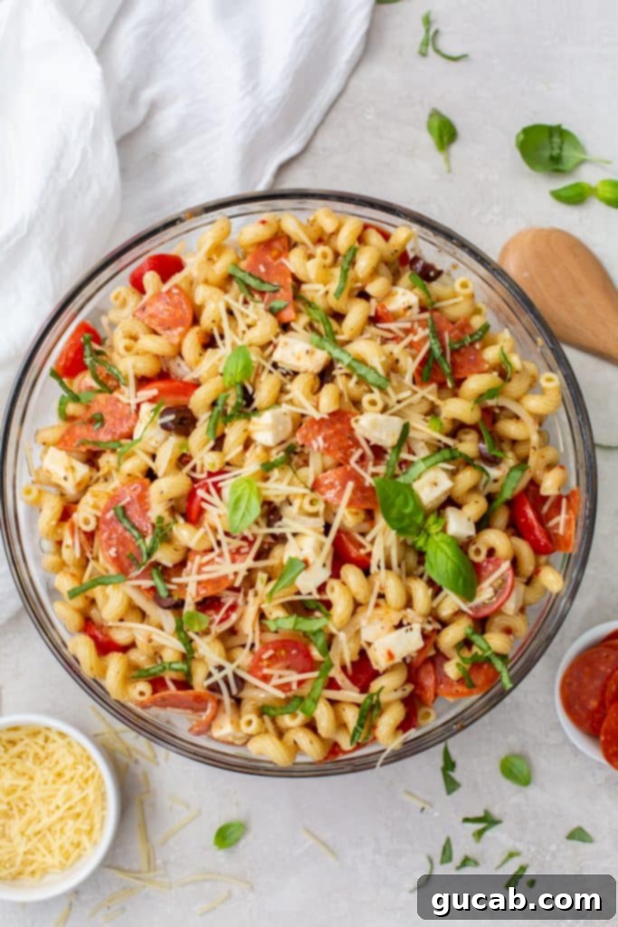 A generous bowl of pizza pasta salad, loaded with pepperoni, cherry tomatoes, mozzarella, and a dusting of Parmesan cheese.