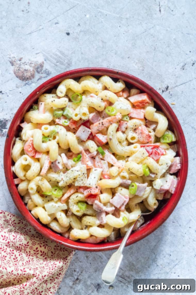 A festive bowl of Hawaiian pasta salad, featuring elbow macaroni, diced ham, sweet pineapple, and colorful bell peppers in a creamy dressing.