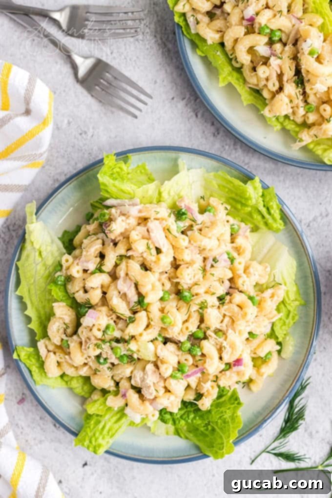 A hearty portion of tuna pasta salad served on a bed of fresh lettuce, featuring macaroni, tuna, celery, and peas.