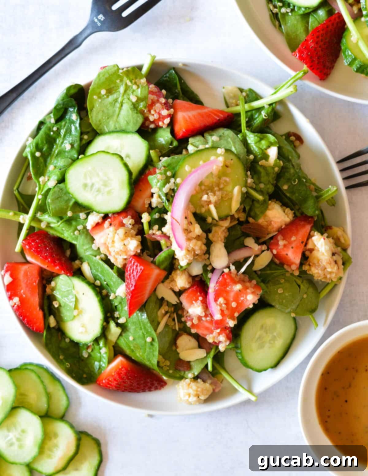 Vibrant spinach salad featuring fresh strawberries, crisp cucumber, homemade pickled onions, and wholesome quinoa, tossed with a light dressing.