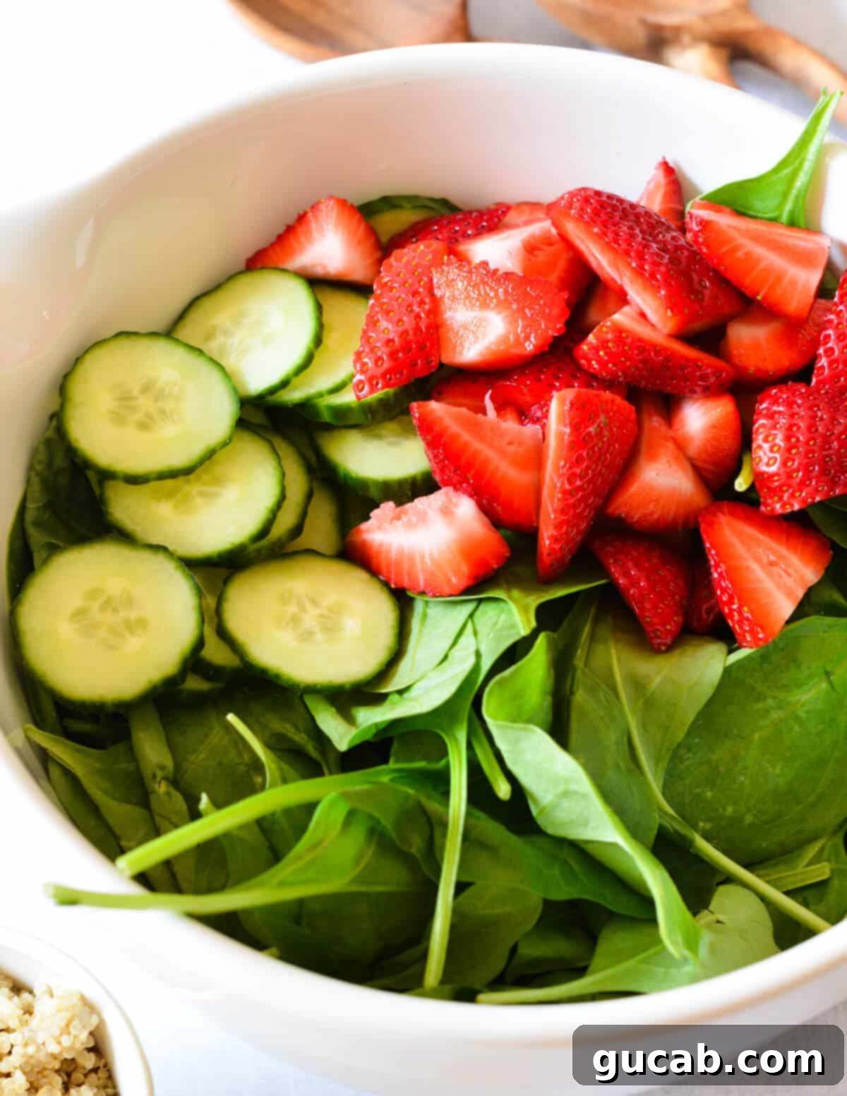 Freshly cut strawberries and thinly sliced cucumber resting atop a bed of crisp spinach leaves in a bowl, ready for additional ingredients.