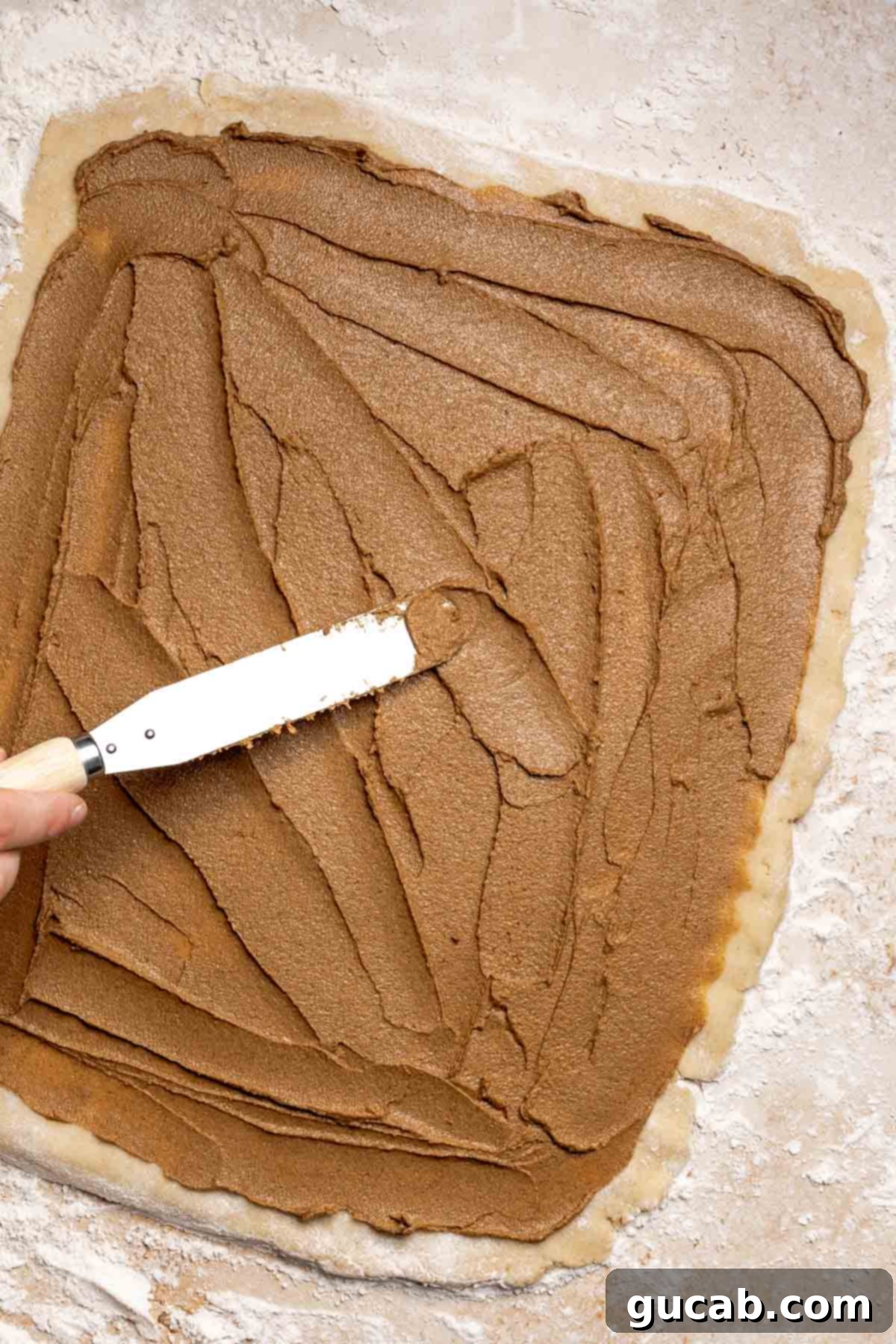 Irresistible Gluten-Free Cinnamon Rolls 15 An offset spatula spreading the softened cinnamon butter filling evenly over the rolled-out gluten-free dough.