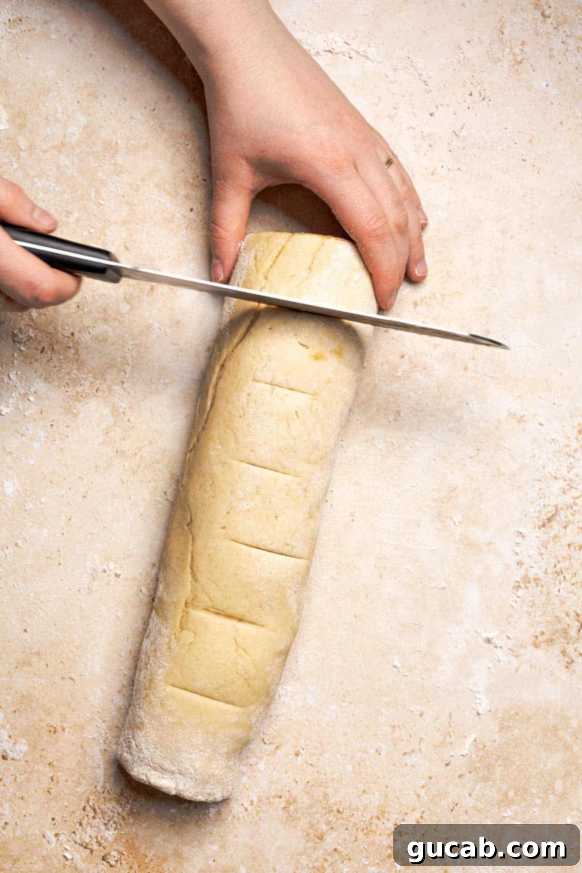 Irresistible Gluten-Free Cinnamon Rolls 17 A hand holding a sharp knife positioned above the rolled gluten-free dough log, ready to cut it into individual cinnamon rolls.