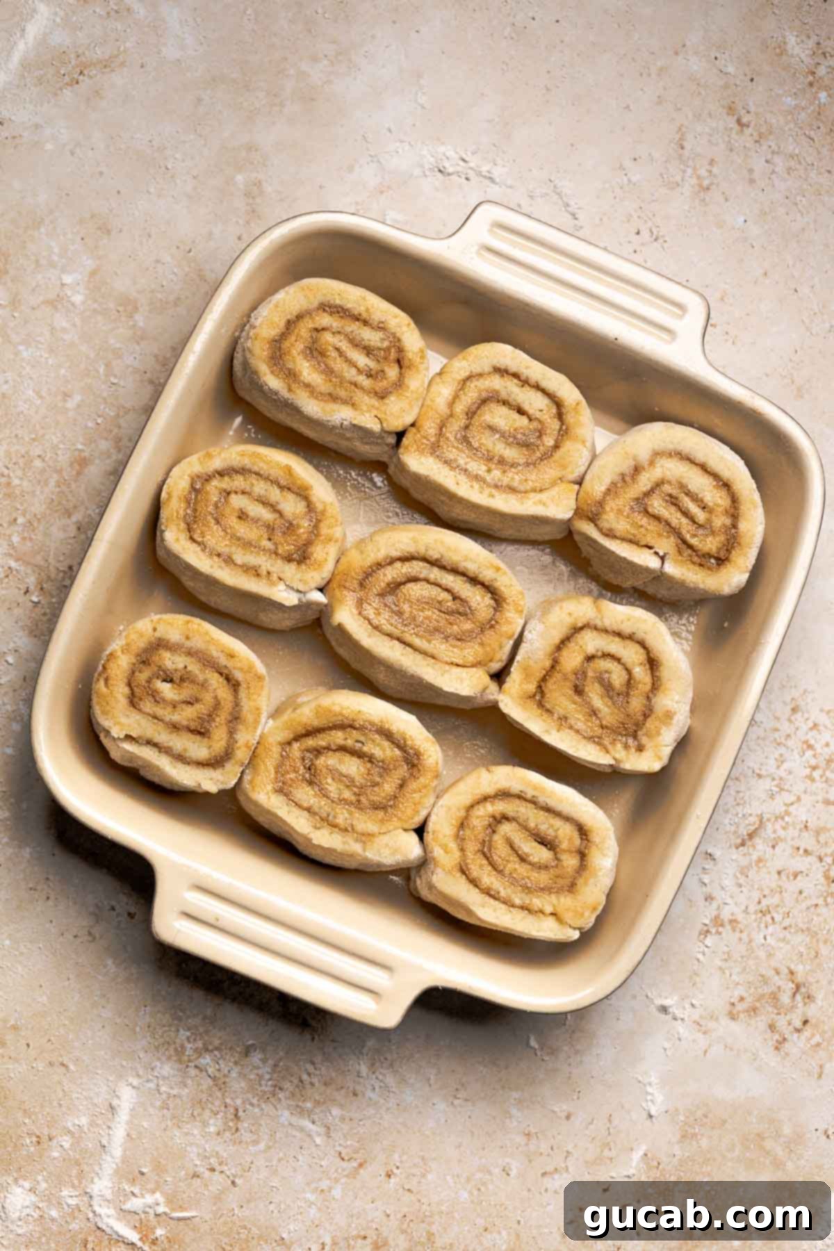 Irresistible Gluten-Free Cinnamon Rolls 19 Unbaked and unrisen gluten-free cinnamon rolls arranged neatly in a greased 8x8 baking dish, ready for their second proof.