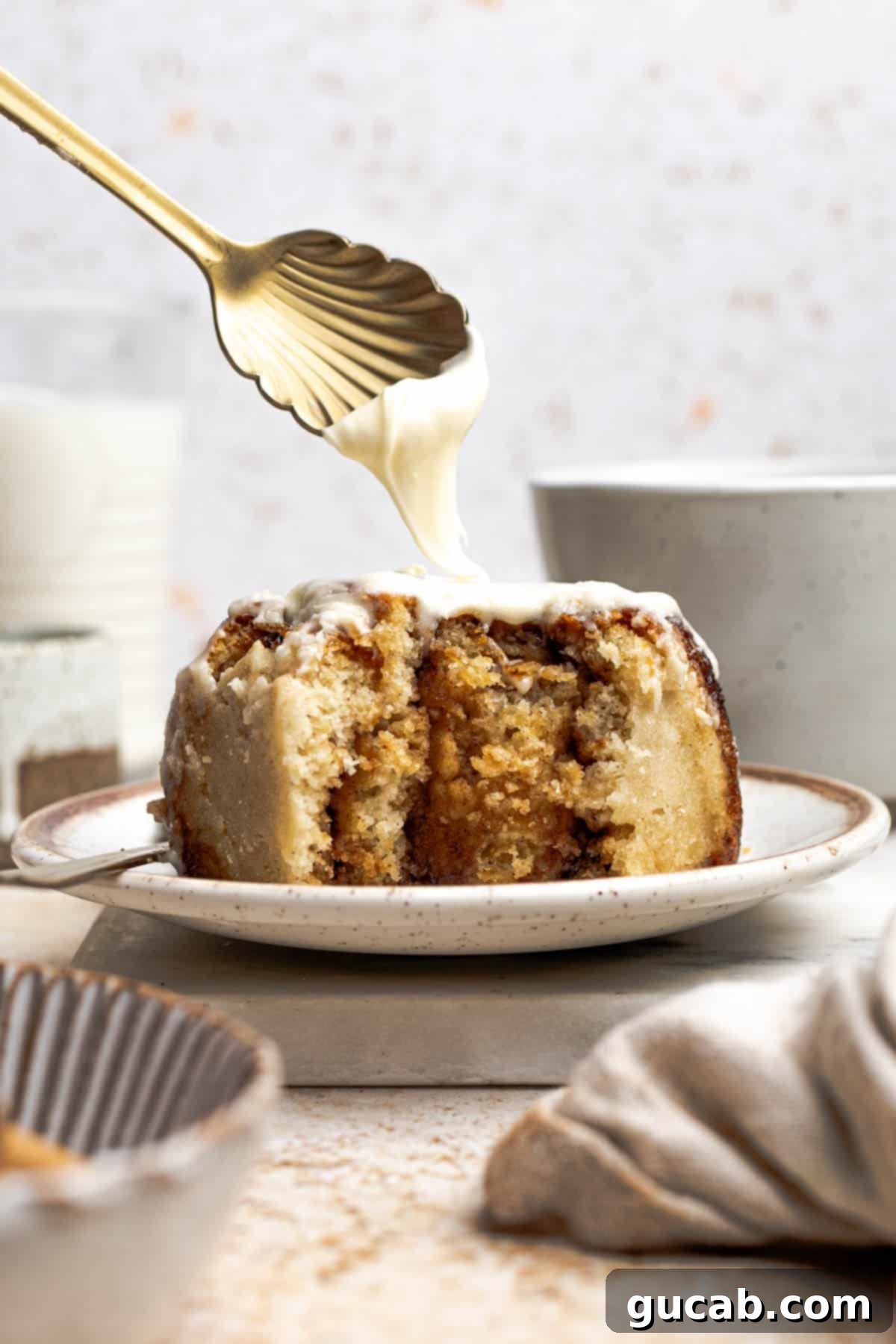 Irresistible Gluten-Free Cinnamon Rolls 3 A spoon delicately drizzling more cream cheese frosting onto a warm, freshly baked gluten-free cinnamon roll.