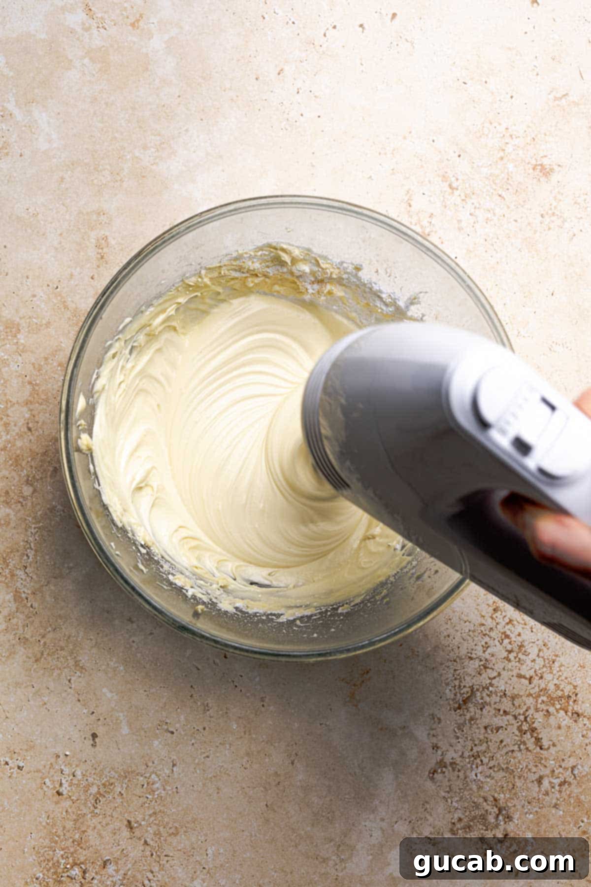 Irresistible Gluten-Free Cinnamon Rolls 22 A hand mixer blending ingredients for a smooth cream cheese frosting in a bowl, showing the consistency of the frosting.