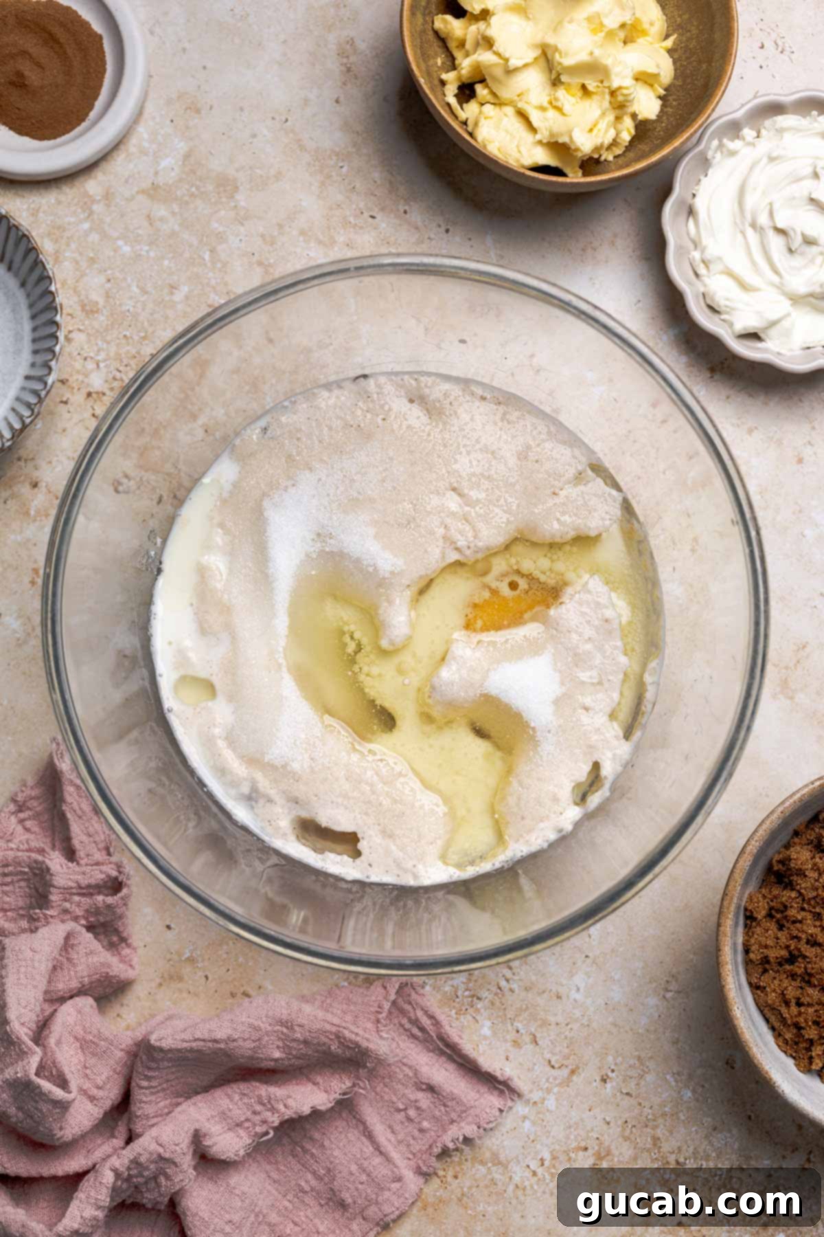 Irresistible Gluten-Free Cinnamon Rolls 7 A bowl filled with the liquid ingredients: milk, frothy yeast, room temperature eggs, sugar, and vegetable oil, before being whisked.