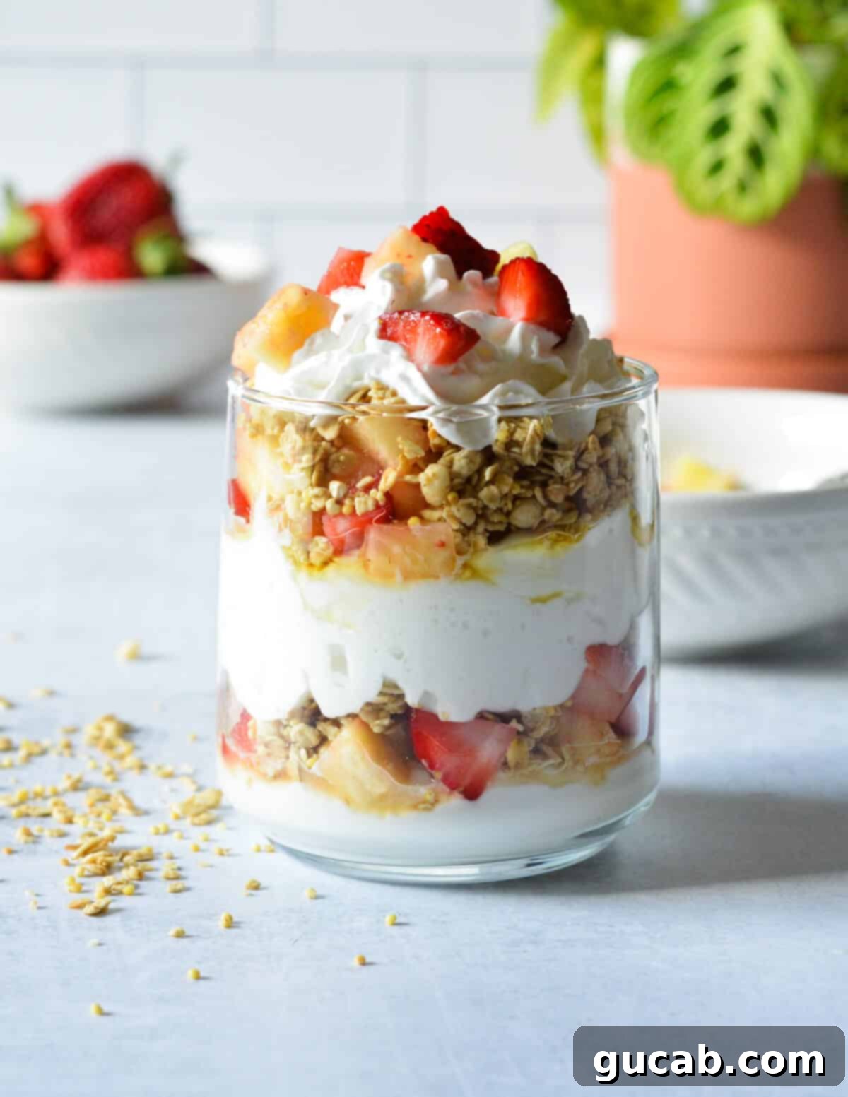 A beautifully layered strawberry pineapple yogurt parfait, topped with fresh fruit and whipped cream, ready to be enjoyed.