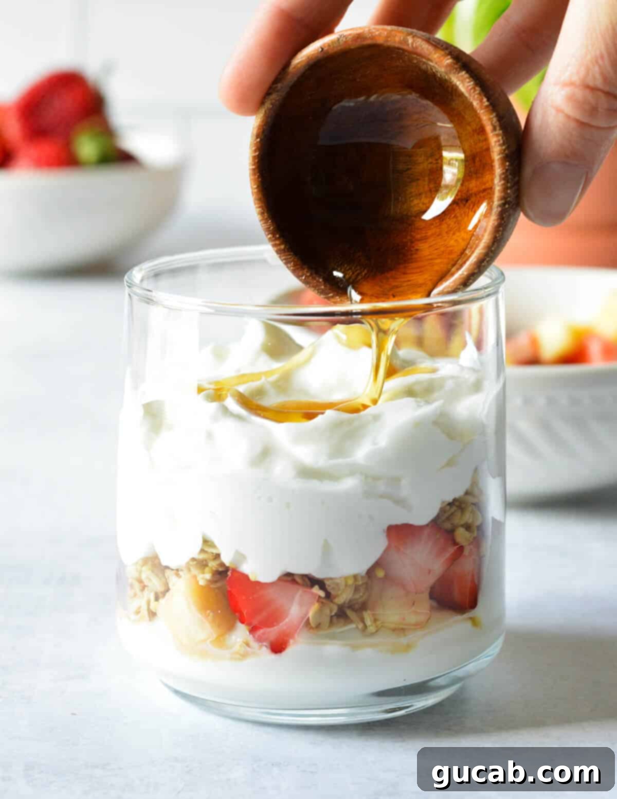 A final drizzle of golden honey being added to the very top of a beautifully layered yogurt parfait, enhancing its natural sweetness.