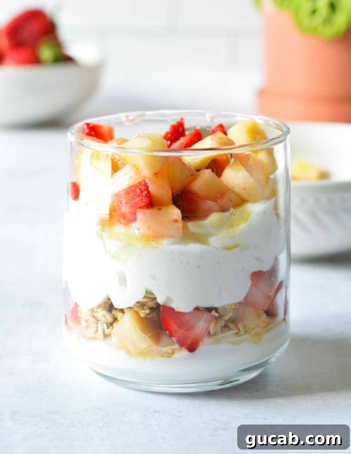 A fully assembled yogurt parfait, showcasing visible layers of Greek yogurt, vibrant strawberries, and golden pineapple, ready to eat.