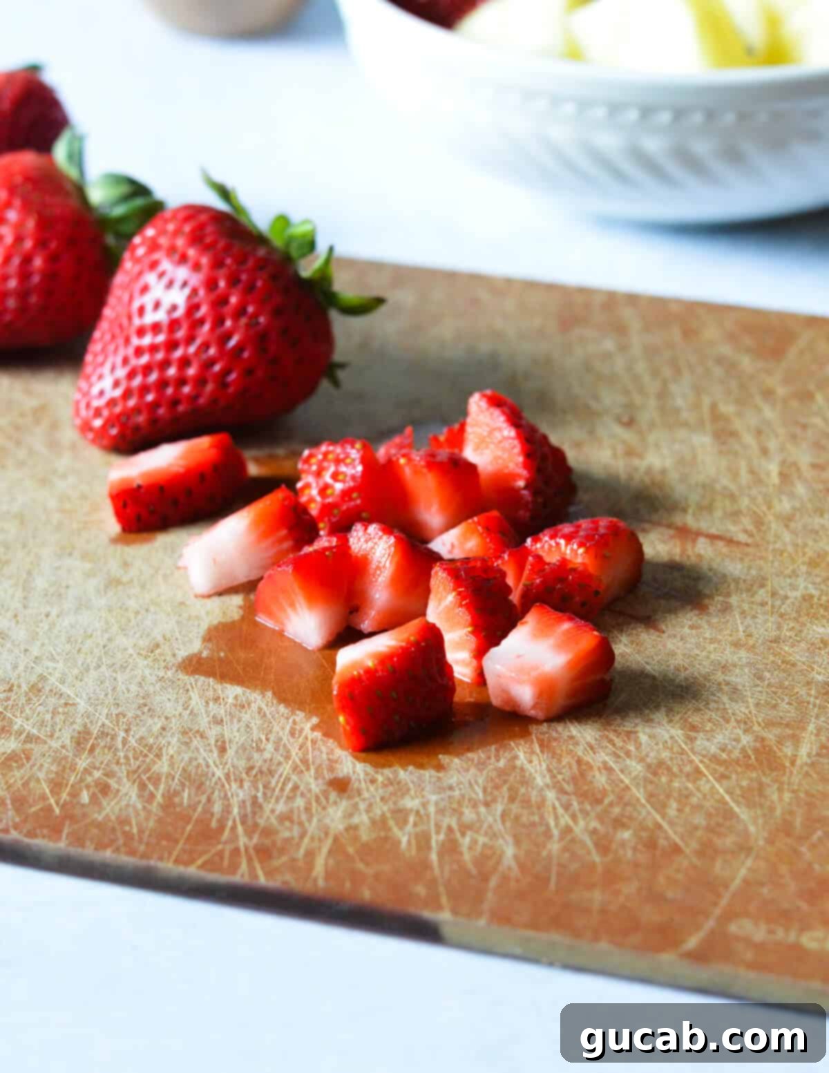 Close-up of fresh, ripe strawberries cut into small, even pieces on a cutting board, ready for a yogurt parfait.