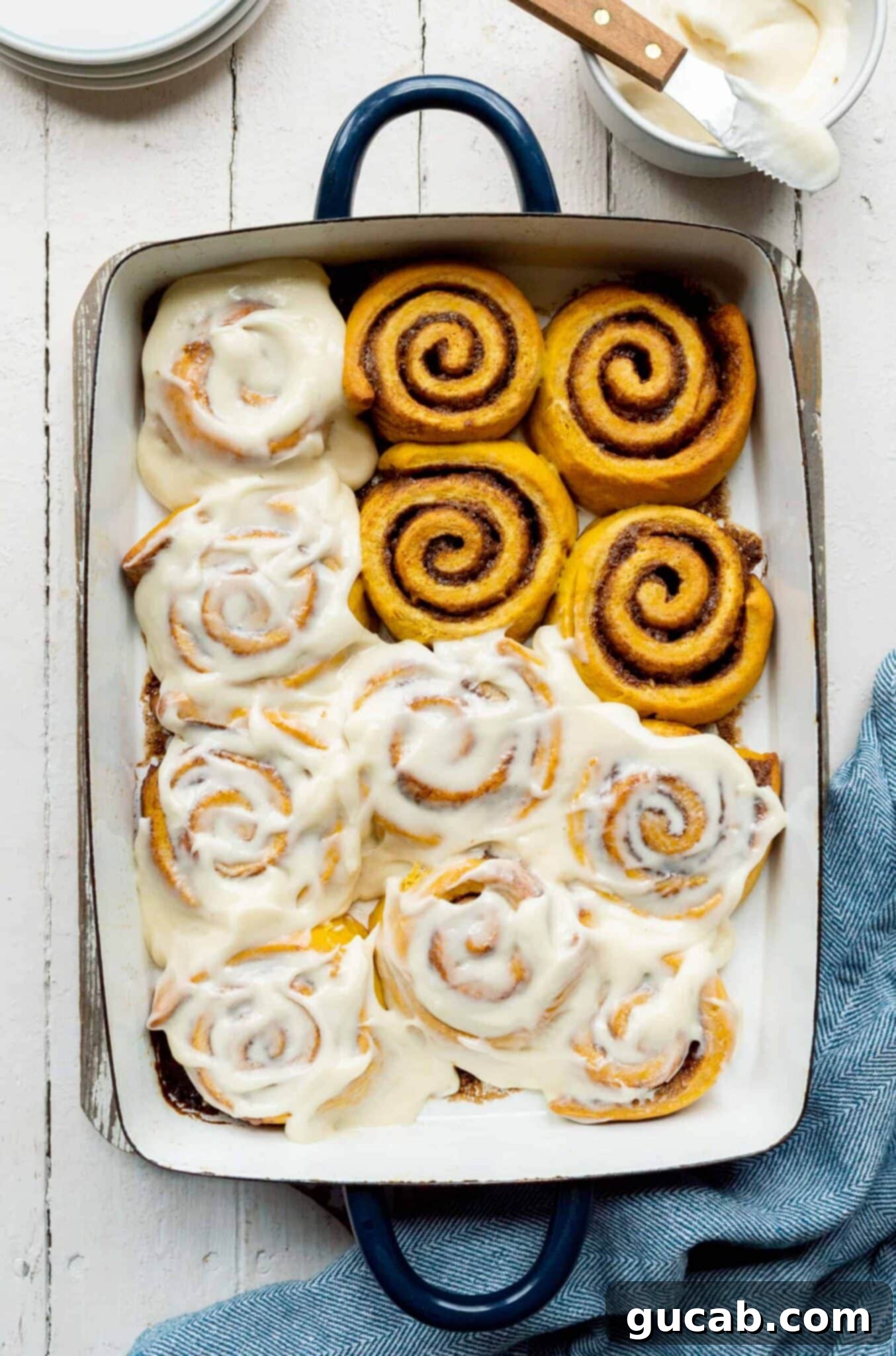 pumpkin cinnamon rolls in a baking dish with cream cheese frosting. 