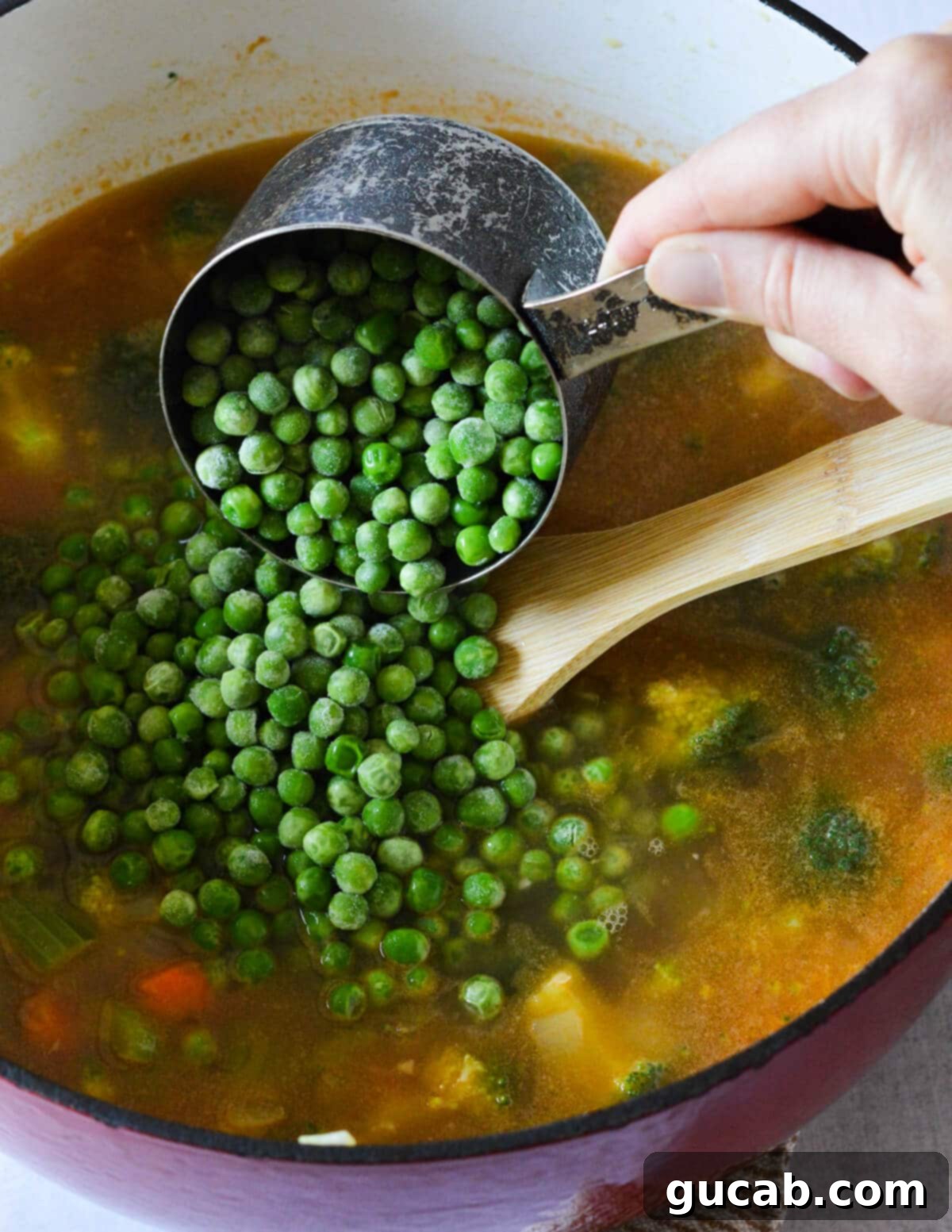 Vibrant Veggie Noodle Bowl 7 Fresh frozen peas being gently poured into a simmering pot of vibrant vegetable soup.