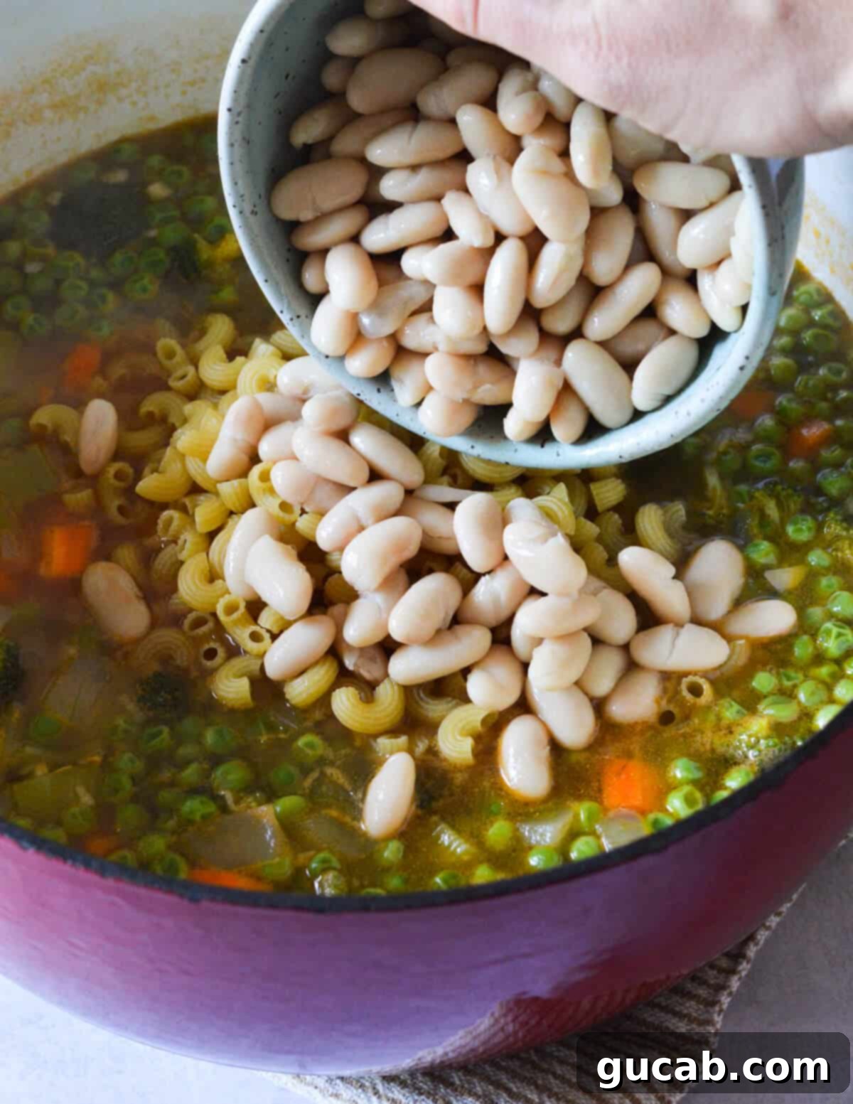Vibrant Veggie Noodle Bowl 9 A bowl of drained cannellini beans being added to the pot of vegetable soup for added protein and creamy texture.