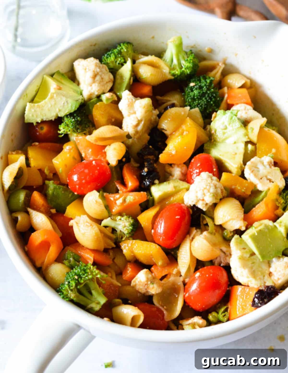 Dawn's Delightful Plant-Based Pasta Toss 2 A large bowl of colorful pasta salad featuring shell pasta, grape tomatoes, broccoli florets, cauliflower, diced bell peppers, and creamy avocado chunks. The salad is beautifully mixed and looks incredibly fresh and appetizing.