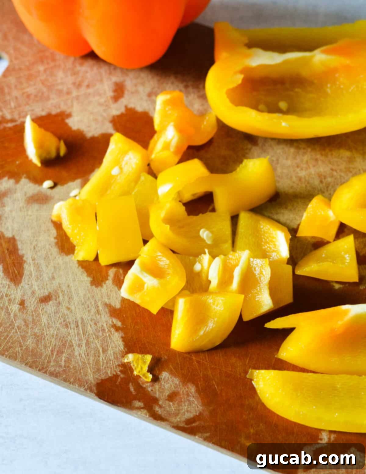 Freshly diced yellow bell peppers on a wooden cutting board, ready for the pasta salad.