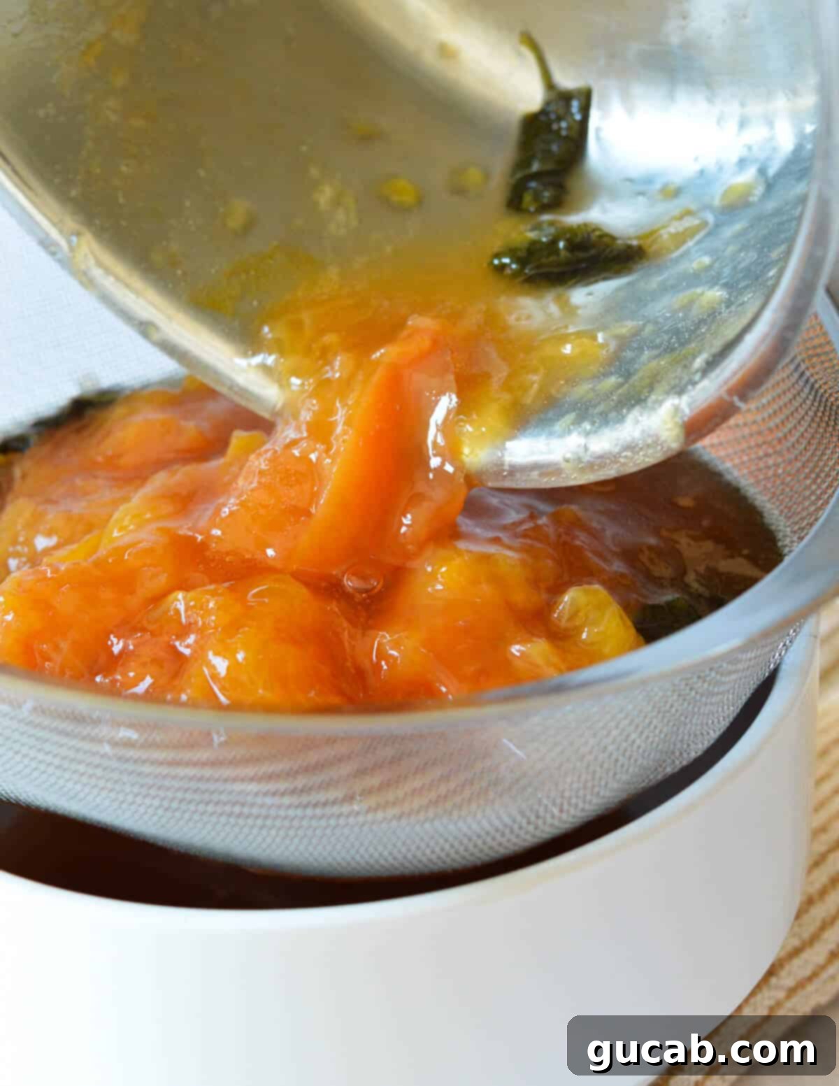 pouring cooked peaches into a fine mesh sieve over a bowl.