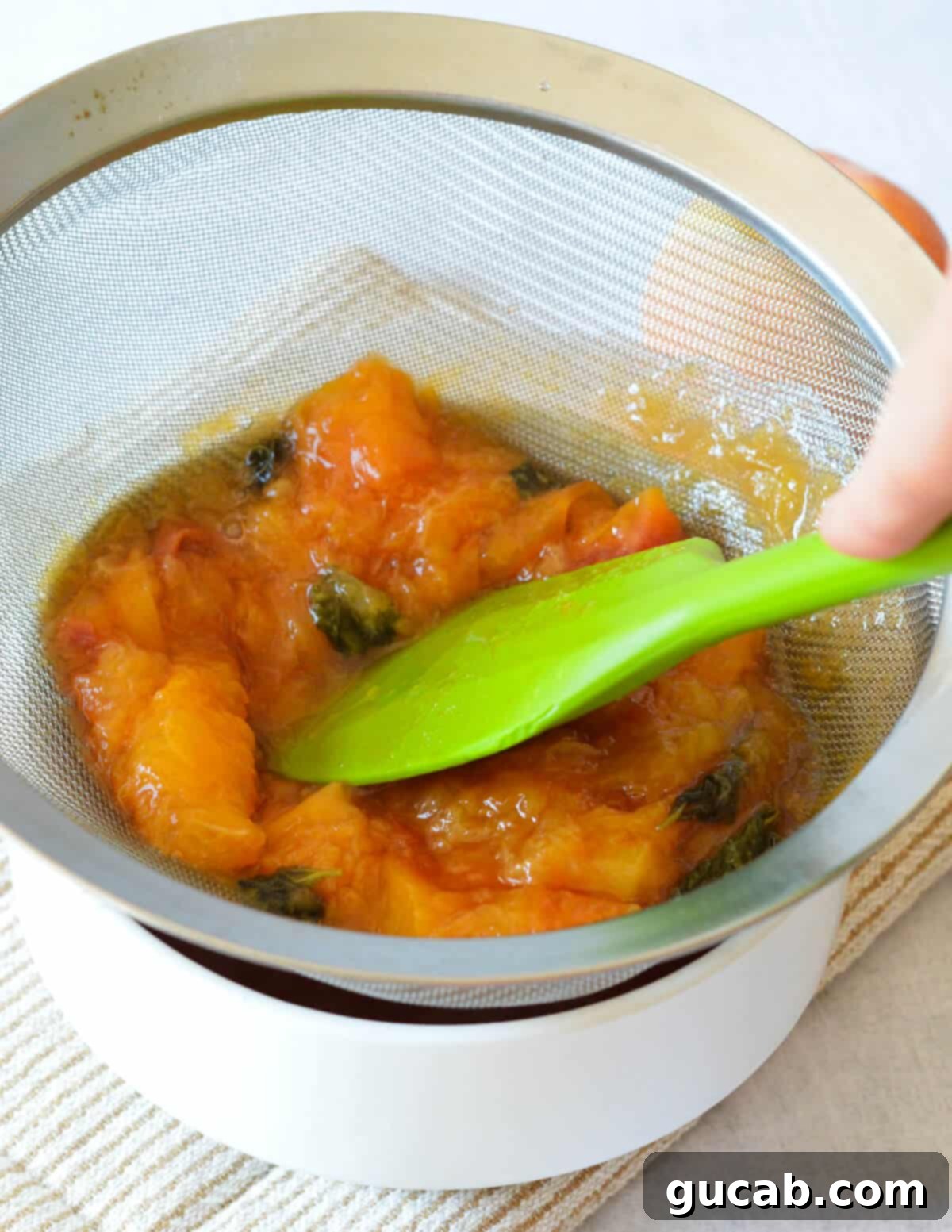 spatula pushing peach mixture through sieve into a bowl. 