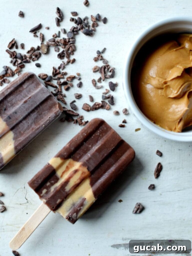 two chocolate banana popsicles next to cocoa nibs and peanut butter