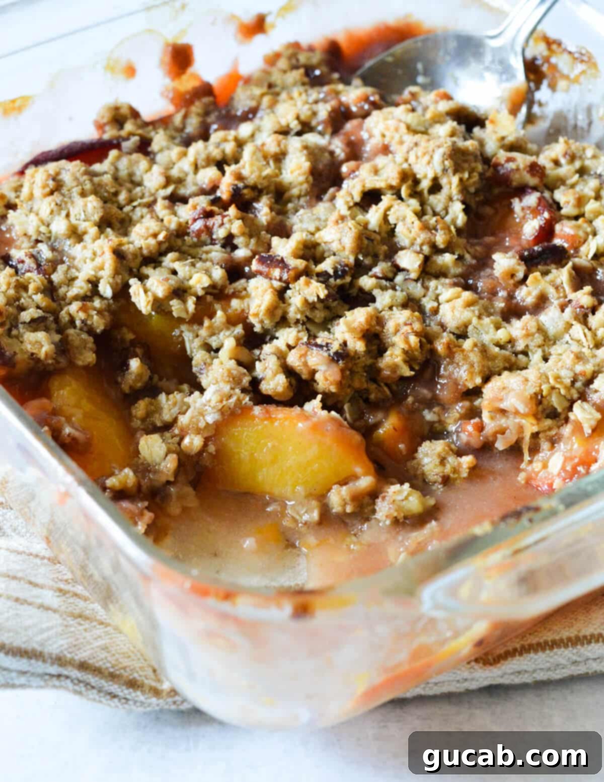A warm, golden brown peach crisp in a baking dish, with a scoop removed, showcasing the juicy peach filling and crunchy oat topping.