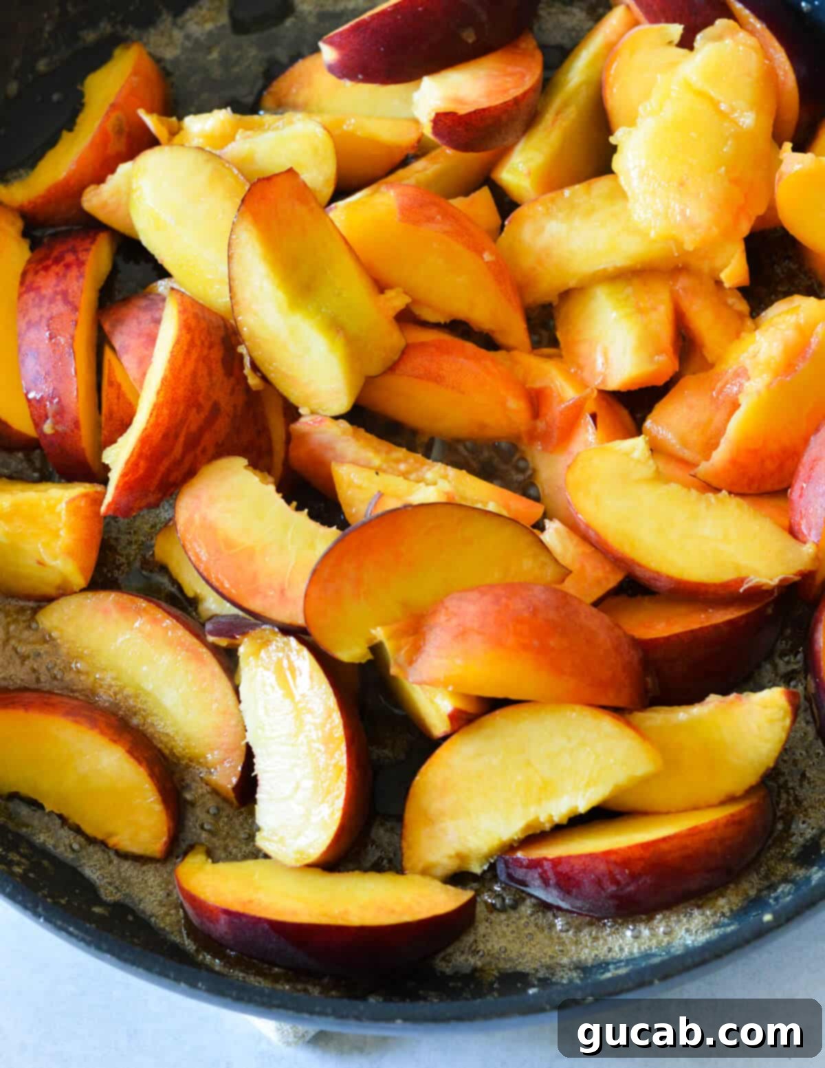 Freshly sliced peaches cooking in a skillet with melted butter and brown sugar, beginning to soften and release juices.