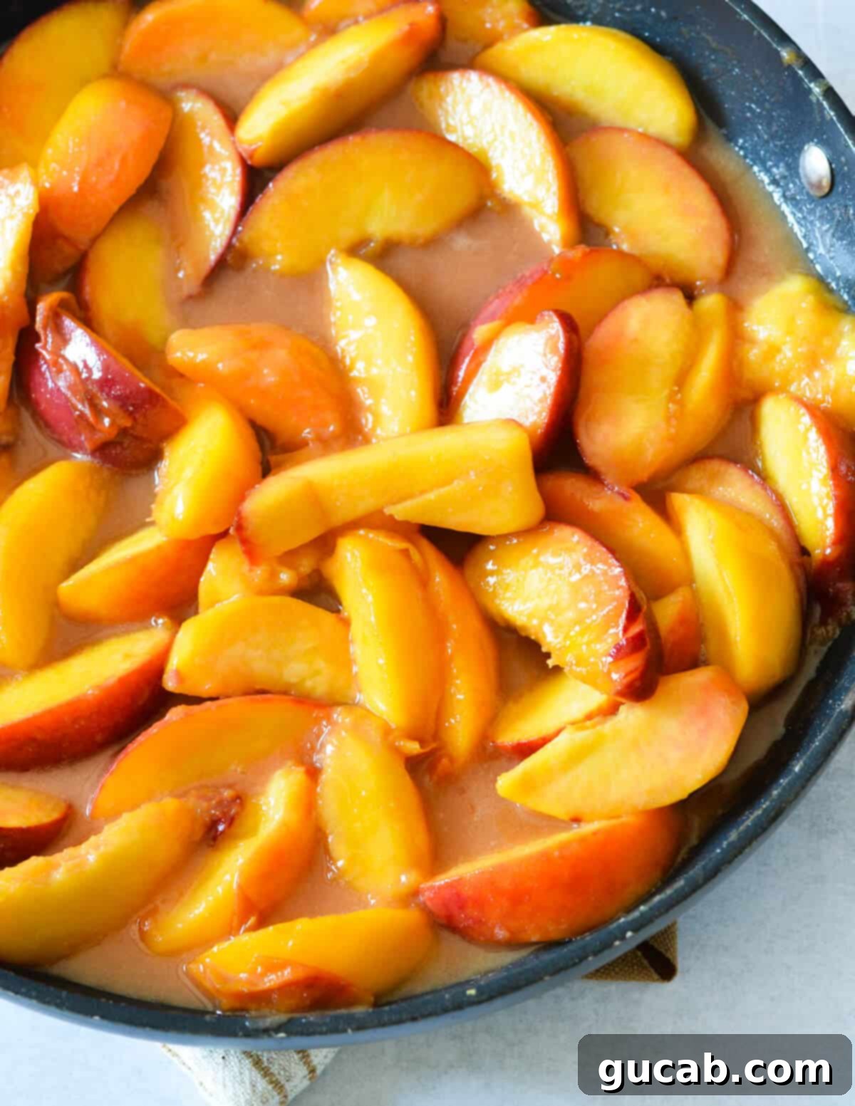 Cooked peach slices simmering in a rich, amber-colored peach sauce in a nonstick skillet, having developed a deeper flavor.