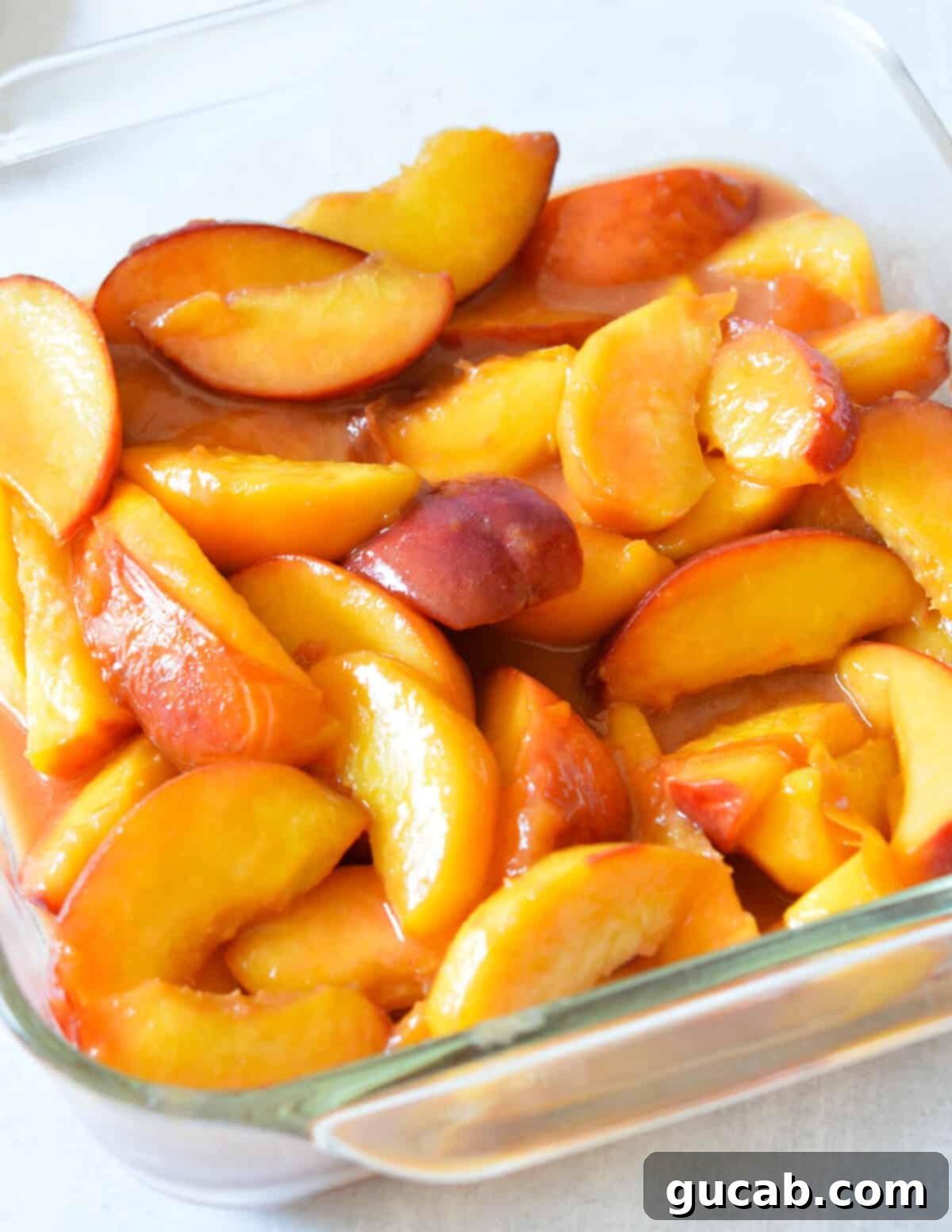 Cooked peach filling poured into a glass baking dish, ready for the crumble topping.