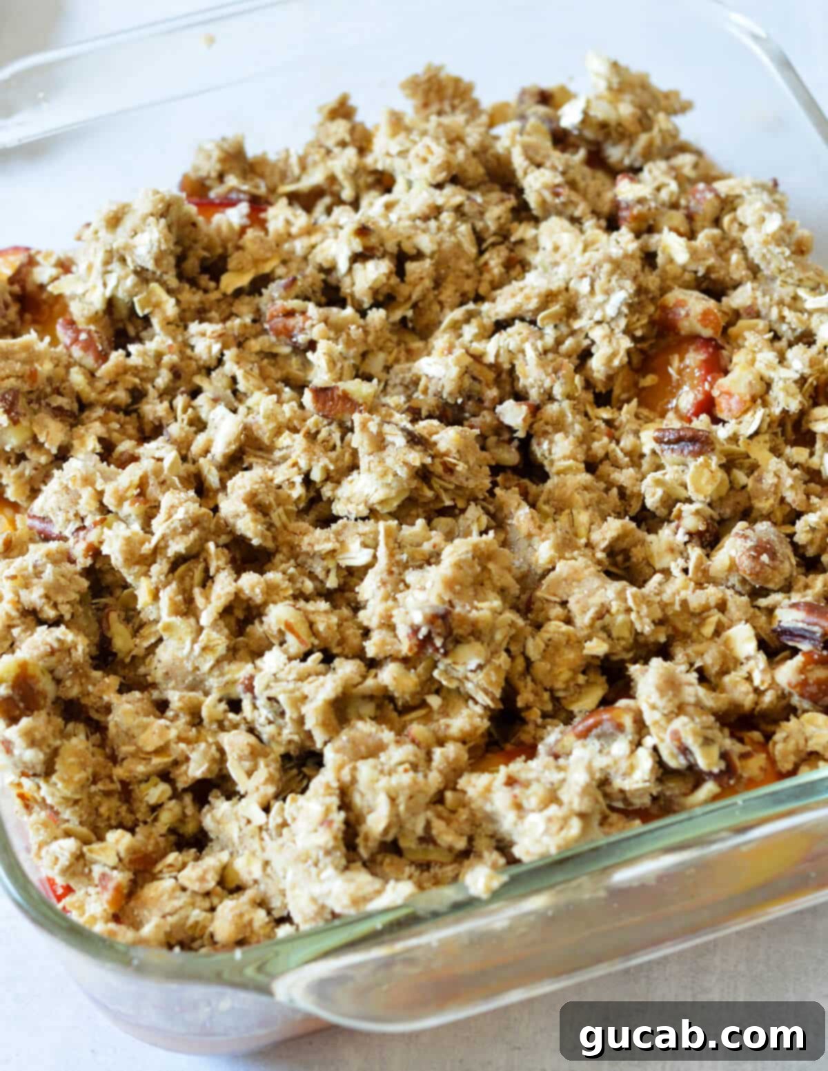 A glass baking dish with peach filling evenly covered with the oat crumble topping, ready for baking.