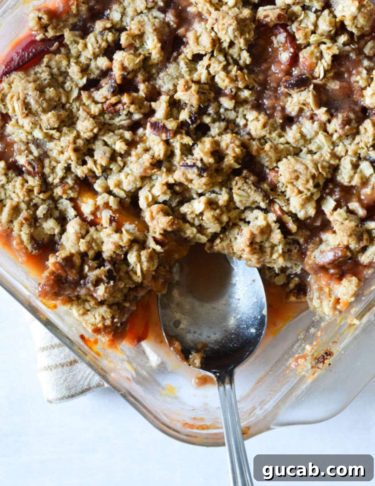A close-up of a warm peach crisp, showcasing the golden-brown oat crumble topping and the bubbling, juicy peach filling underneath, with a spoon resting in the dish.