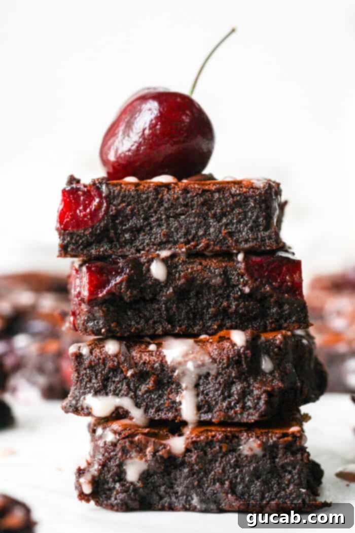 a stack of fudge brownies with cherries in them with a bing cherry on top.
