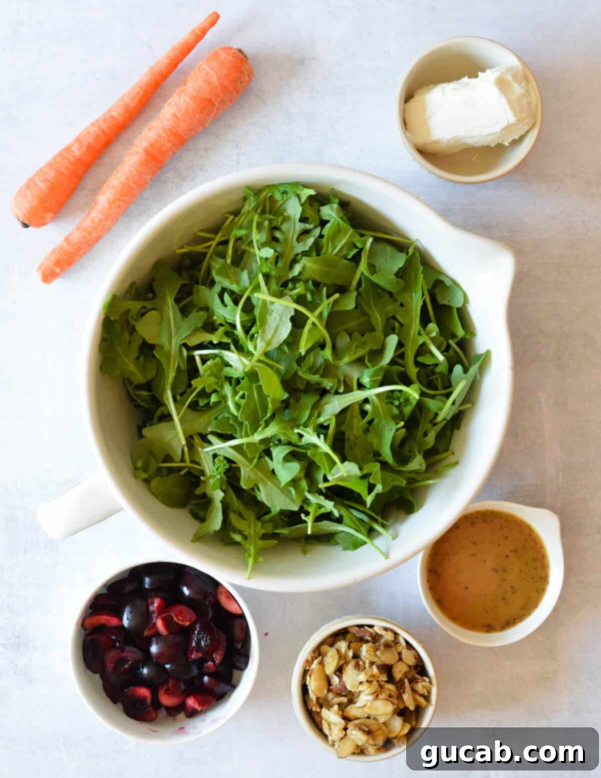 Fresh baby arugula, vibrant red cherries, creamy goat cheese crumbles, thinly shaved carrots, and a bottle of balsamic vinaigrette — the core ingredients for a delicious cherry arugula salad.