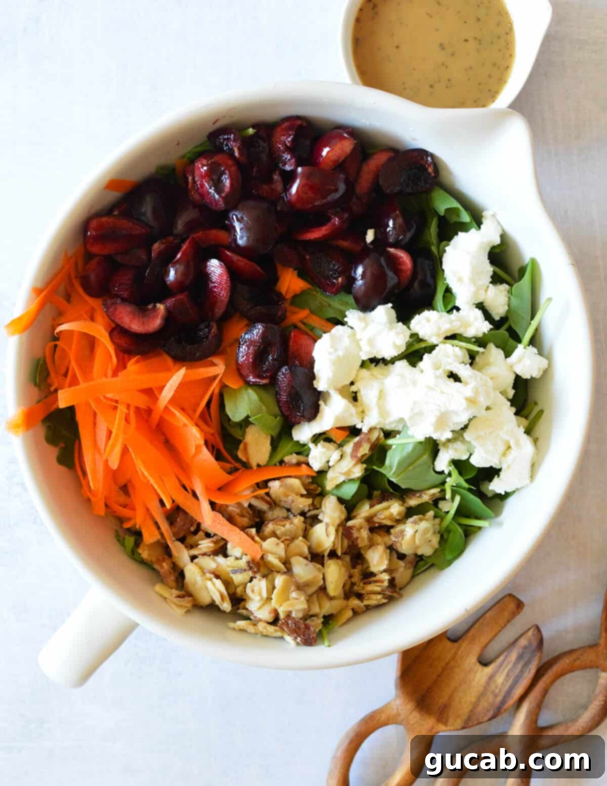 A large, inviting bowl filled with fresh arugula salad, featuring vibrant cherries, thinly shaved carrots, creamy goat cheese, and golden candied almonds, drizzled with balsamic vinaigrette.