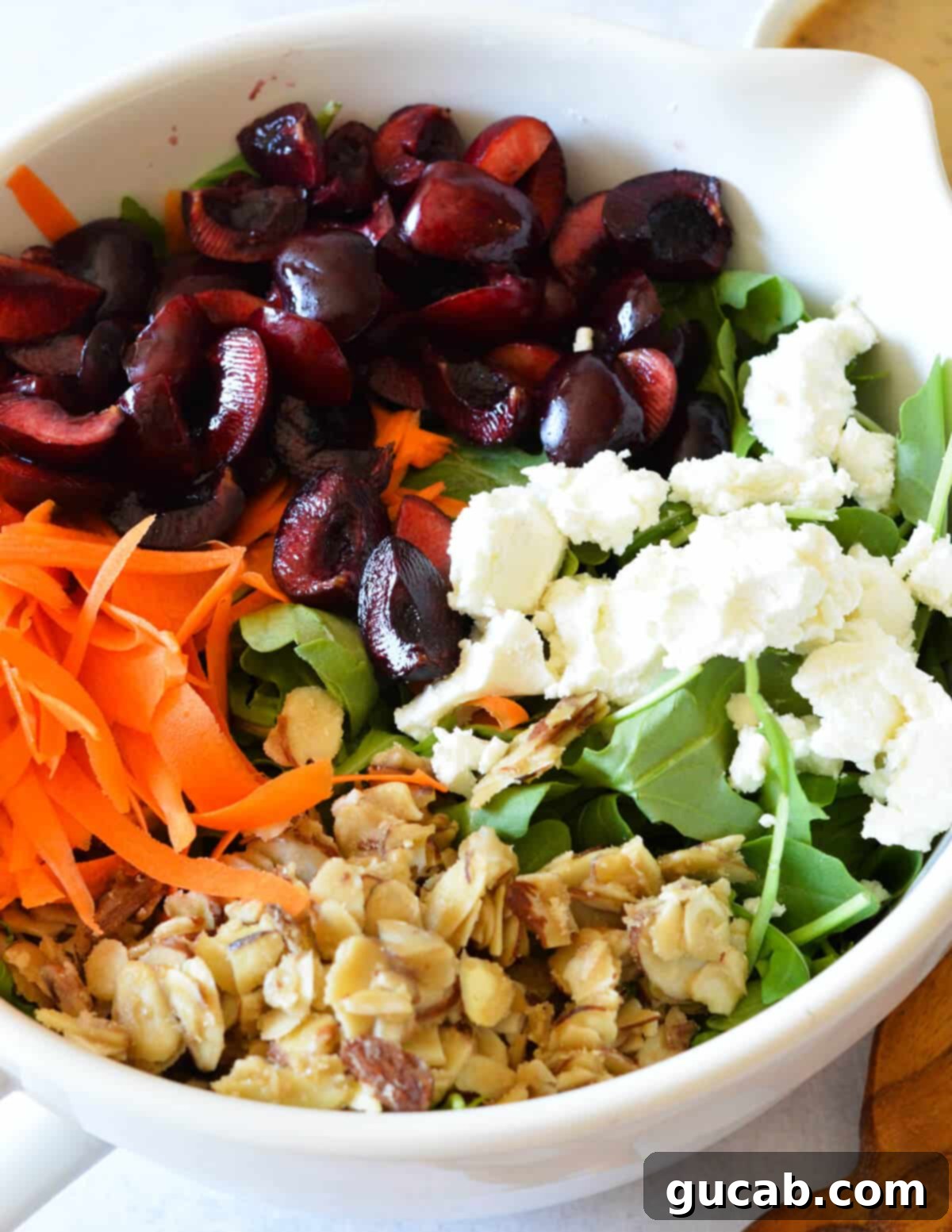 A close-up shot highlighting the intricate textures and colors of the arugula salad: glistening Bing cherries, delicate shaved carrots, golden candied almonds, and fresh, peppery arugula leaves, ready to be served.