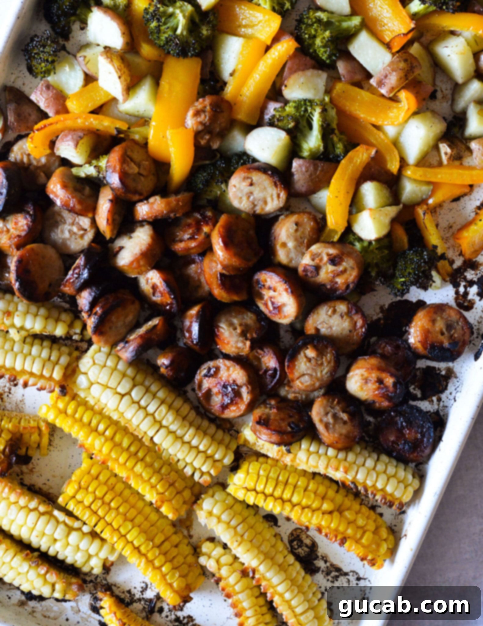 A sheet pan loaded with golden-brown roasted veggies, perfectly caramelized chicken sausage slices, and unique buttered corn ribs, all ready to serve.