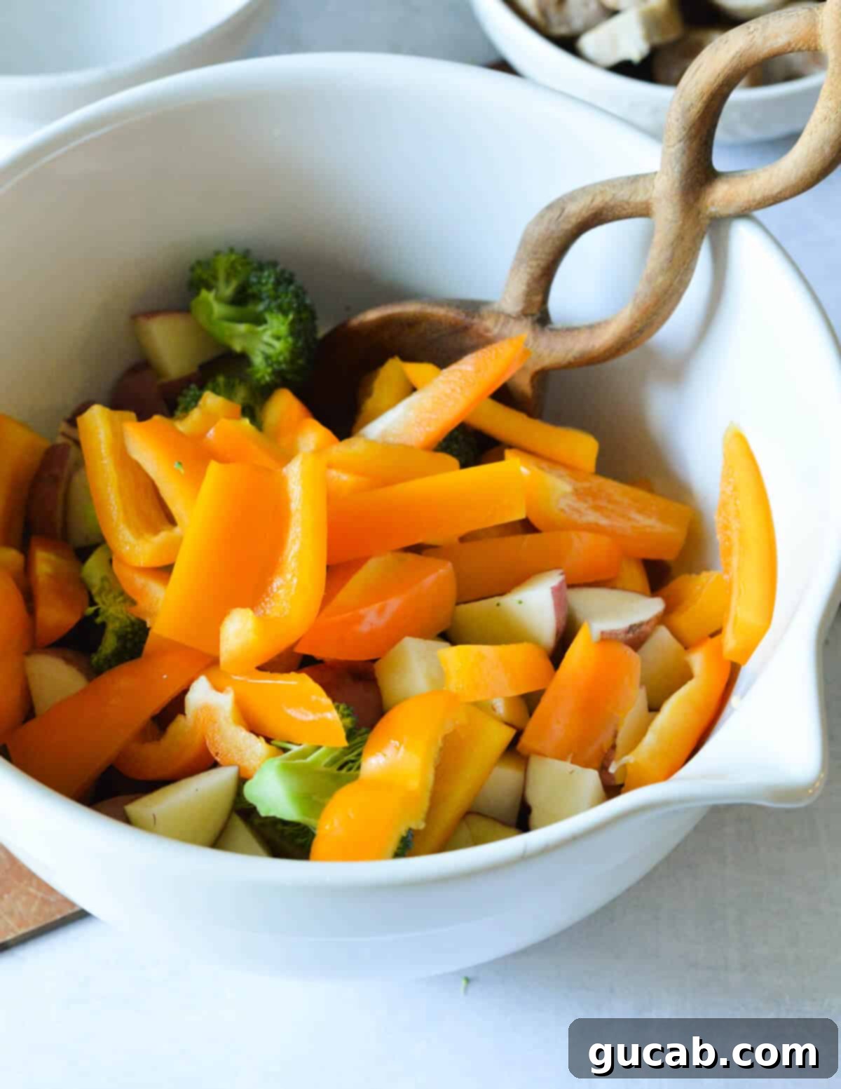 A large bowl containing a colorful mix of sliced orange bell pepper, fresh broccoli florets, and diced potatoes, prepped for roasting.