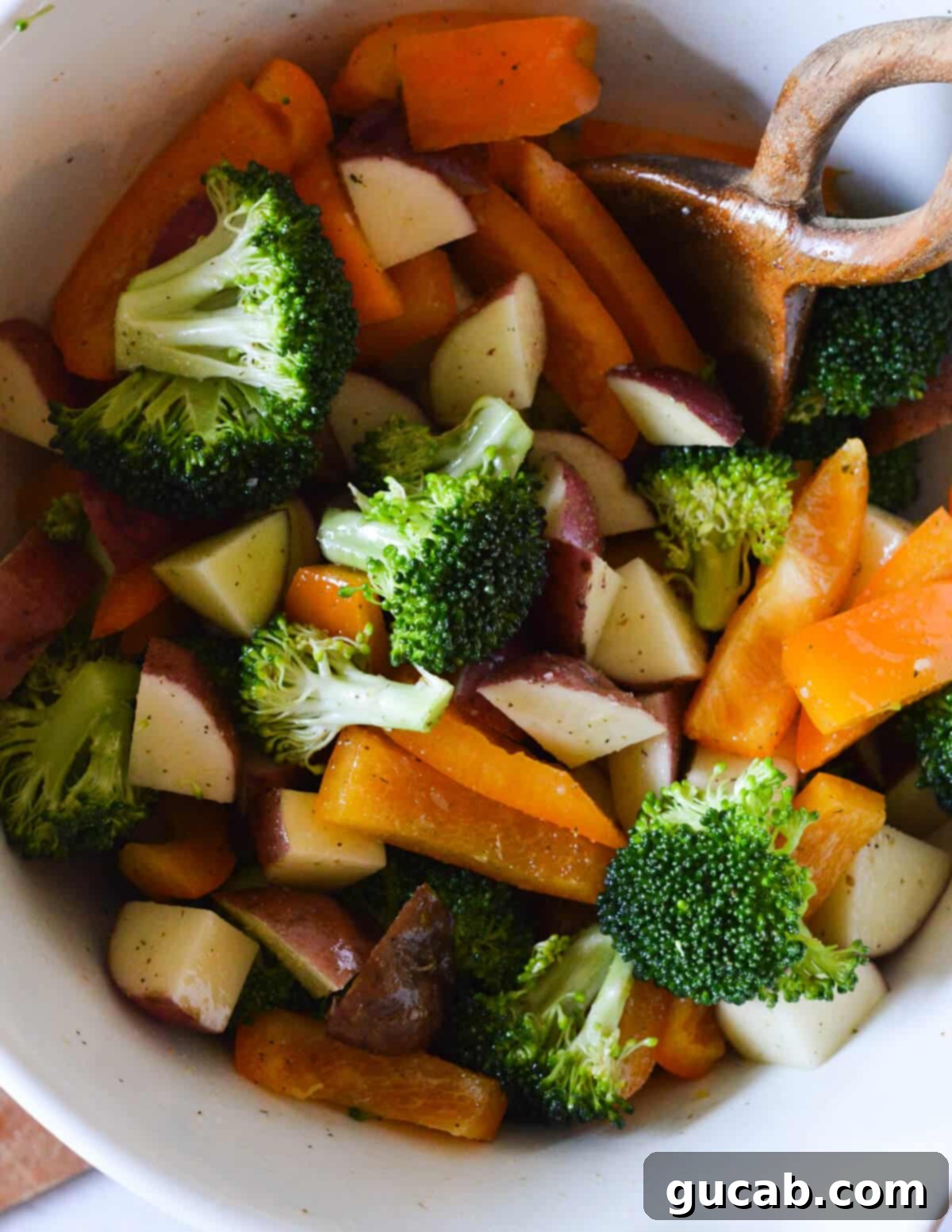 Broccoli florets, bell peppers, and diced potatoes beautifully coated in olive oil and seasonings in a large bowl, ready for the sheet pan.