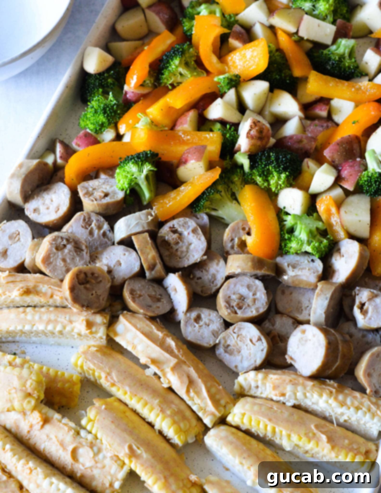 A fully assembled sheet pan ready for the oven, featuring colorful bell peppers, crisp broccoli, diced potatoes, neatly sliced chicken sausage, and buttered corn ribs, all arranged for optimal roasting.
