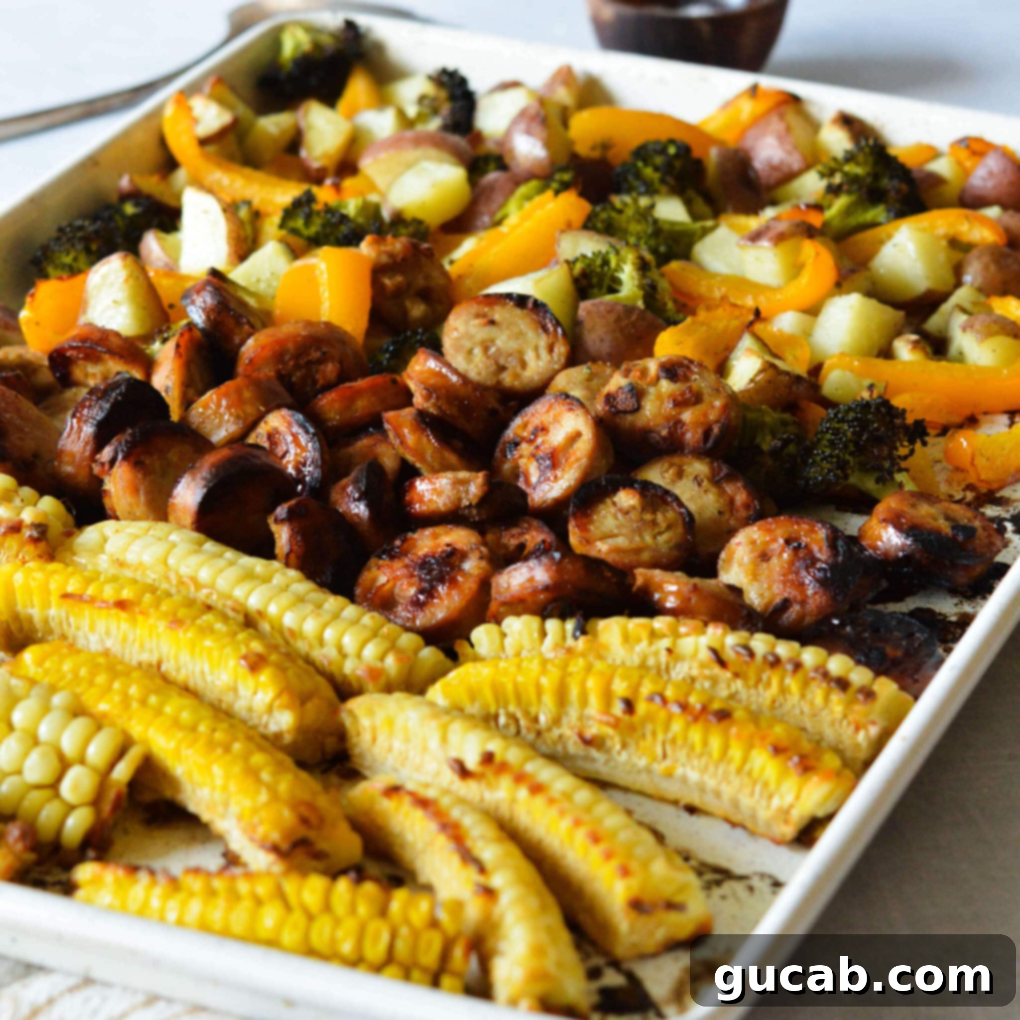 A close-up of the finished chicken sausage sheet pan dinner, showcasing the crispy, curled corn ribs, golden-brown caramelized chicken sausage, and tender, roasted bell peppers, broccoli, and potatoes.