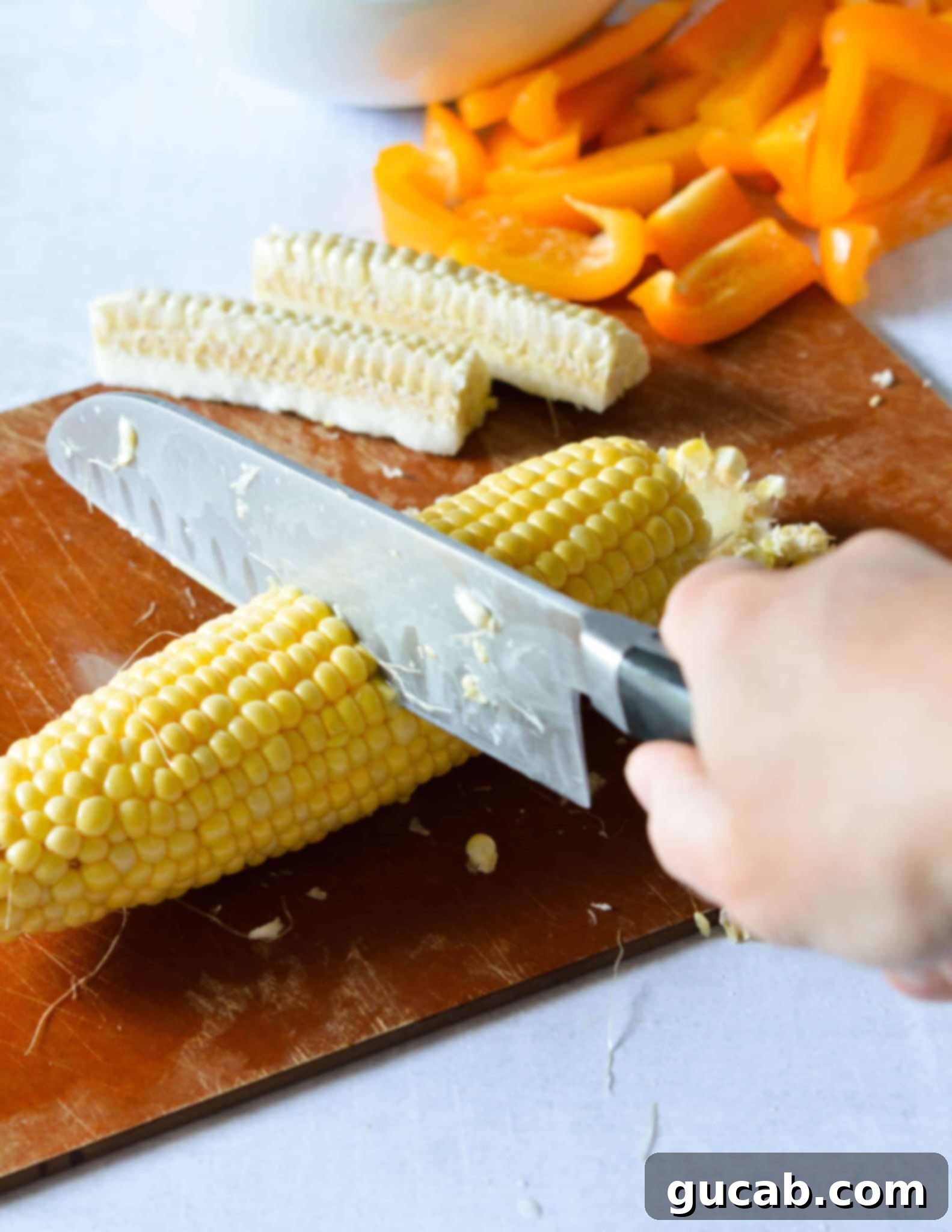 A sharp knife carefully positioned to cut a corn cob in half horizontally, a crucial step for making corn ribs.