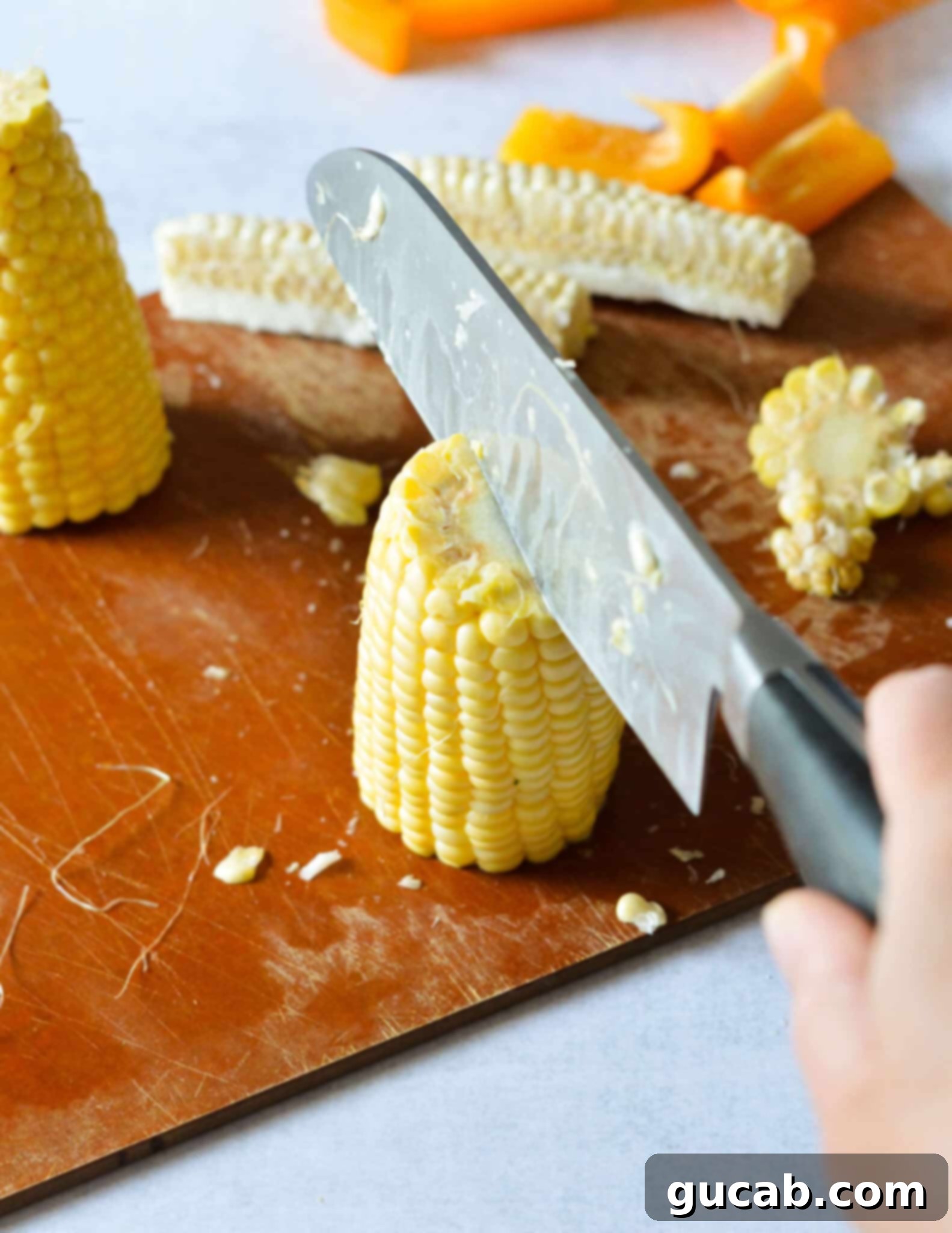 A knife slicing vertically through half a corn cob, splitting it to begin forming corn ribs.