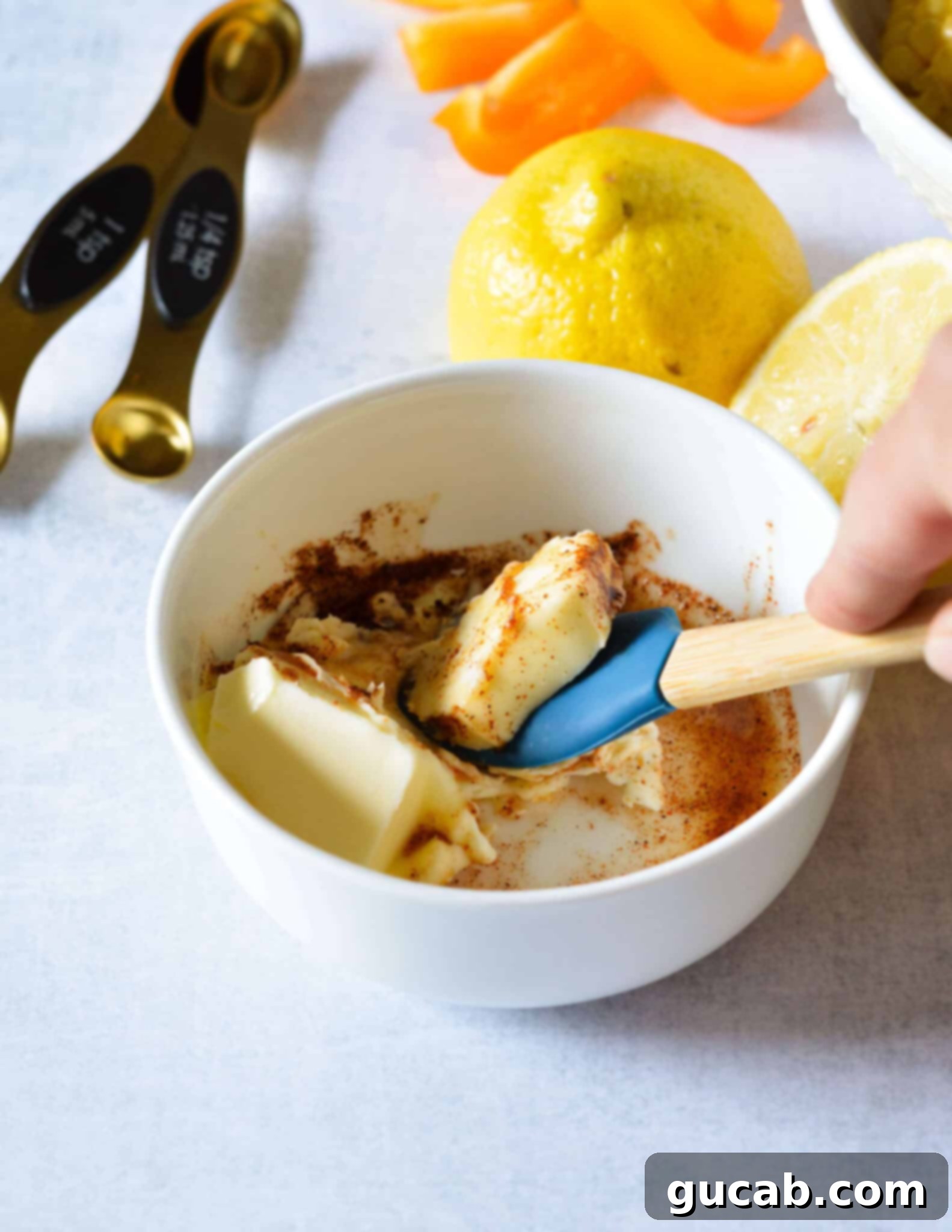 A spatula mixing softened butter with ancho chili powder and fresh lemon juice in a bowl to create a flavorful paste for corn ribs.