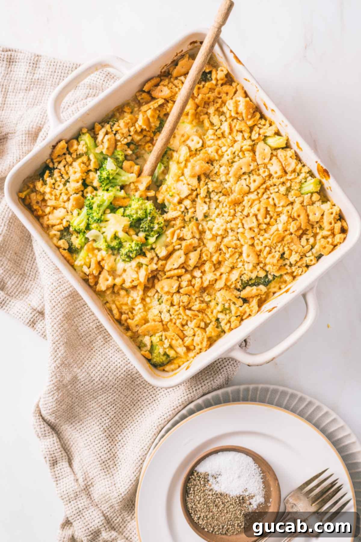 Deliciously Gluten-Free Thanksgiving: 19 Must-Try Recipes 10 A baking dish of golden-brown gluten-free broccoli casserole with a wooden spoon, revealing a creamy, cheesy interior and crunchy topping, a delicious alternative to green bean casserole.