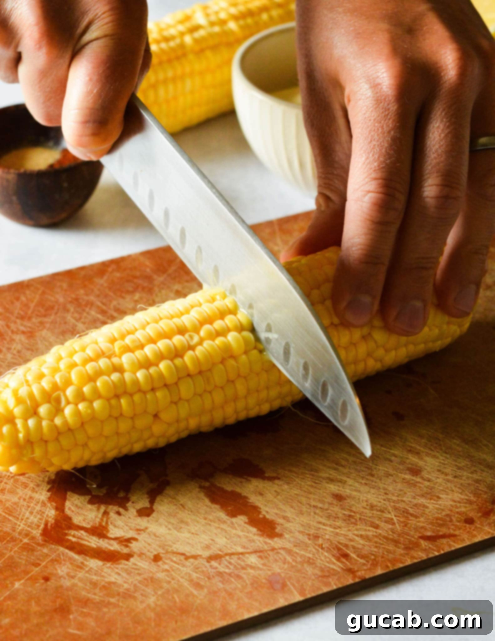 knife cutting a corn cob in half crosswise. 