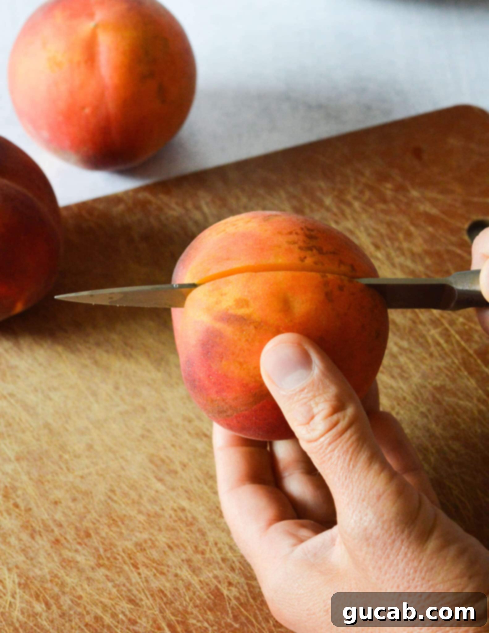 A hand holding a peach and precisely cutting it in half along its natural seam.