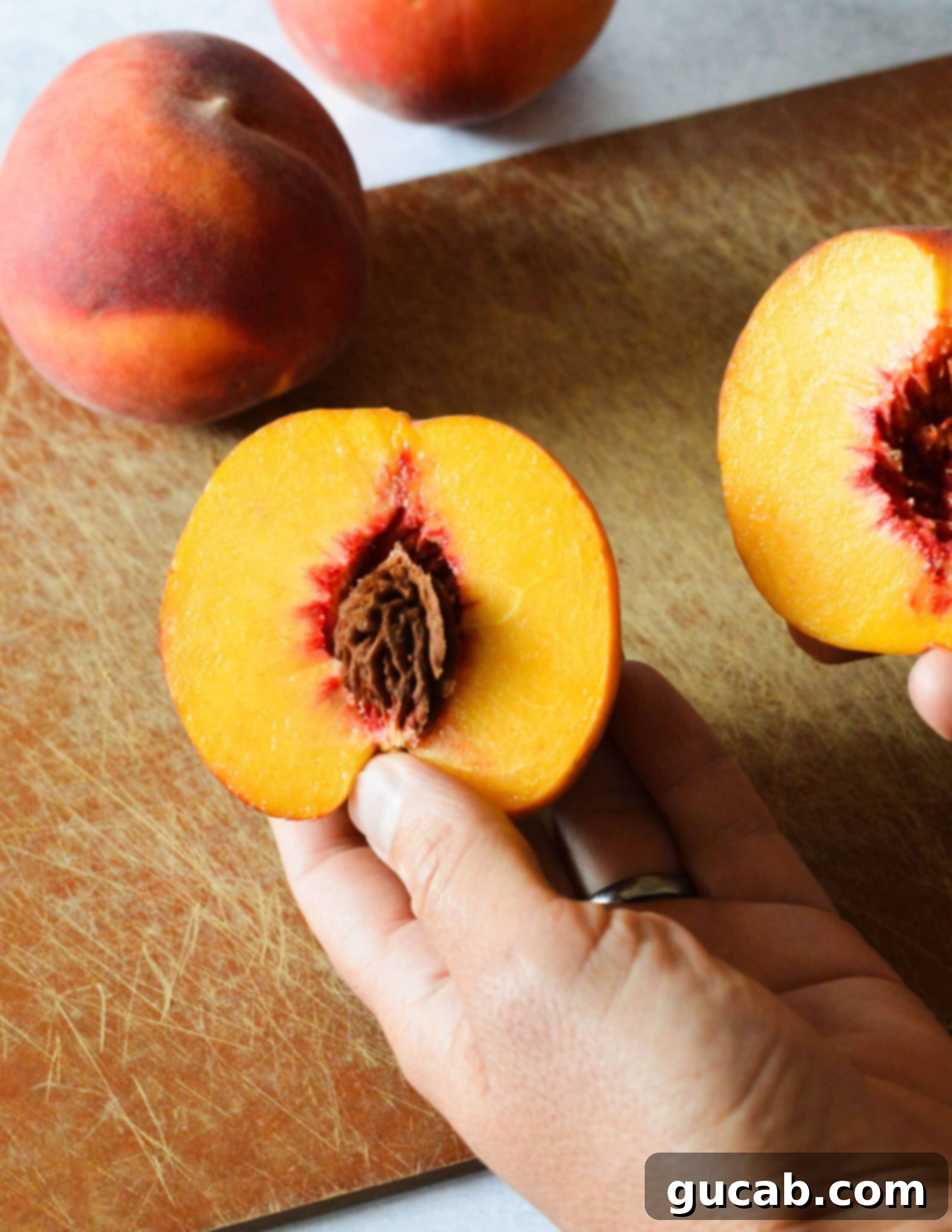 Two hands gently twisting the peach halves apart after cutting.