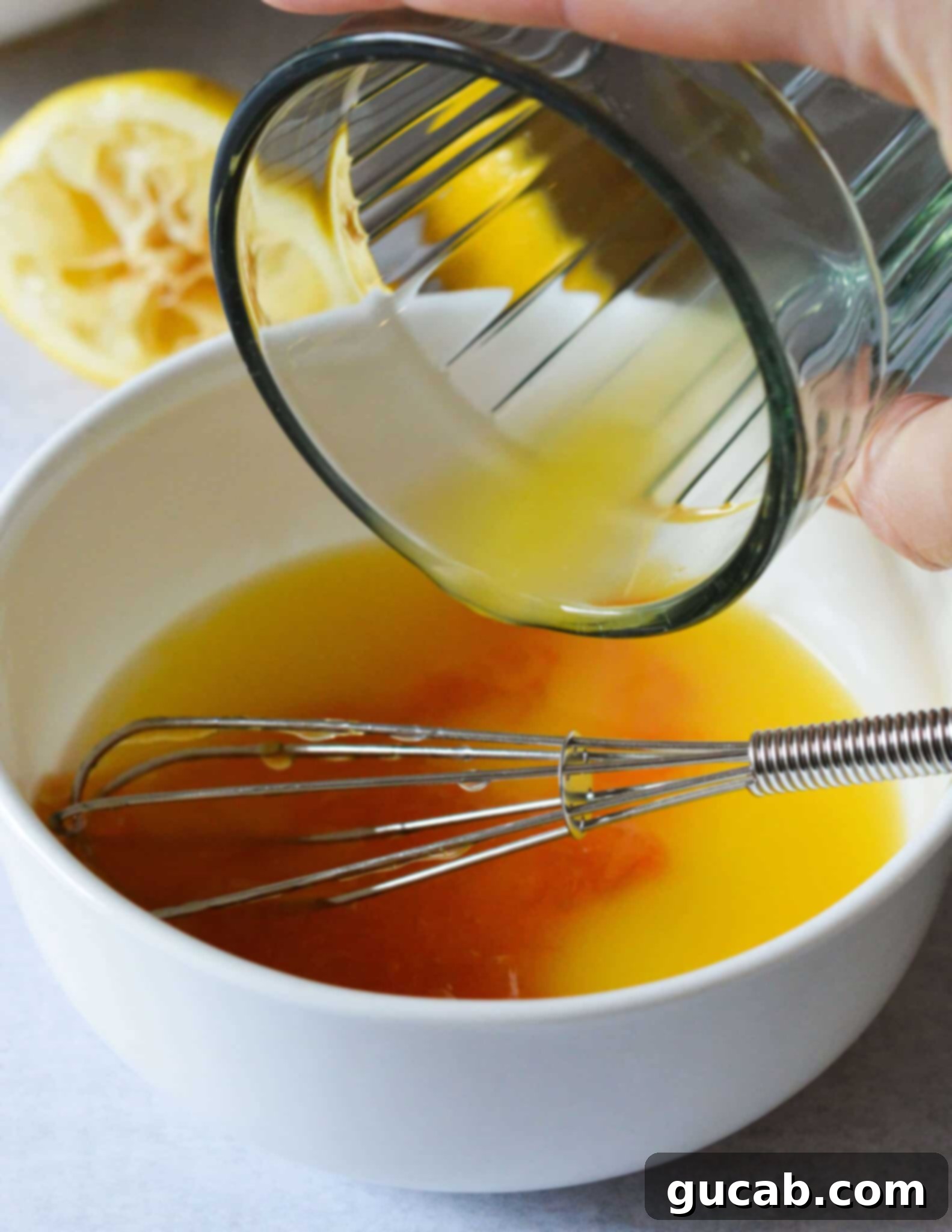 A hand pouring fresh orange juice into a bowl already containing peach jam and lemon juice, preparing the dressing.