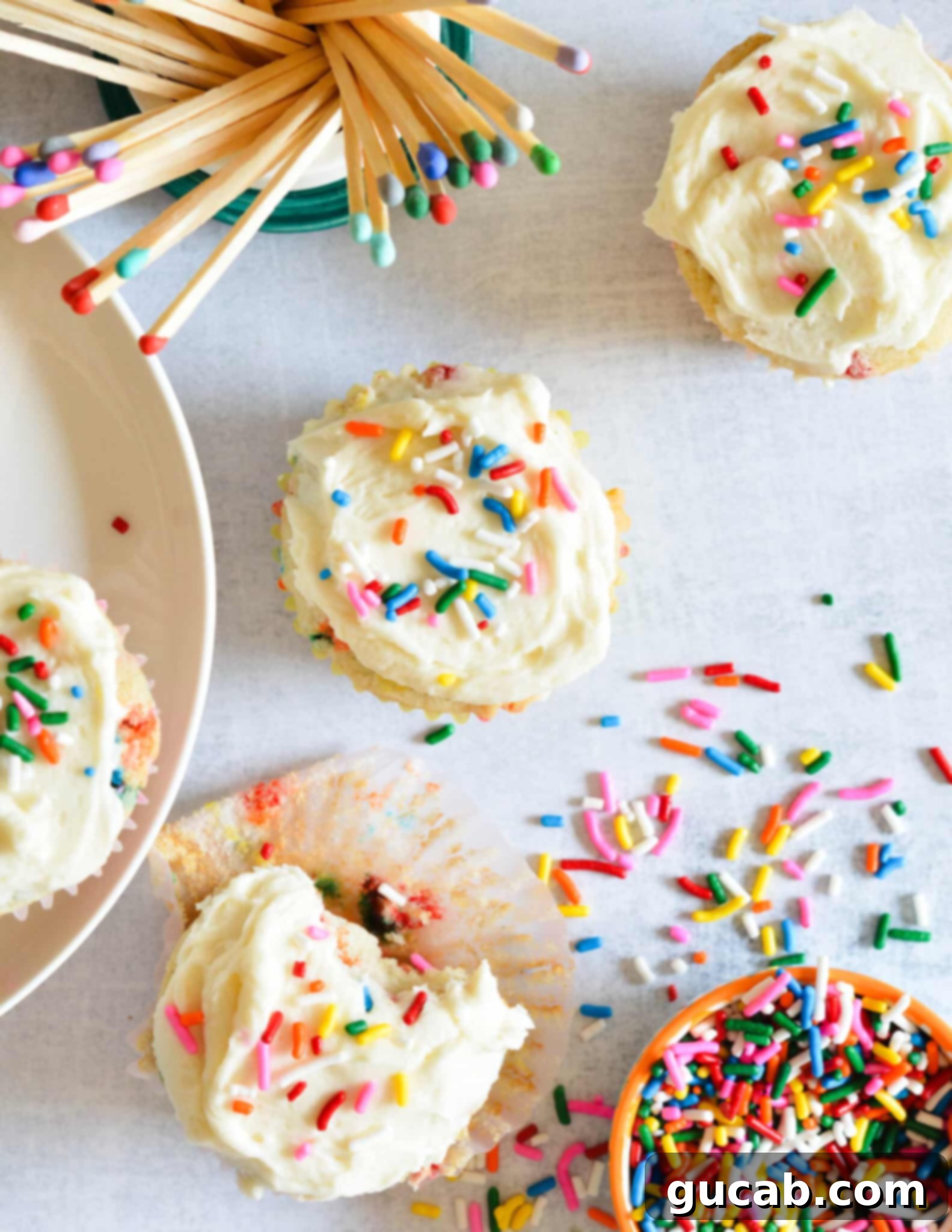 A cluster of freshly baked gluten-free funfetti cupcakes, a bowl of colorful sprinkles, and decorative matches, setting a festive mood.