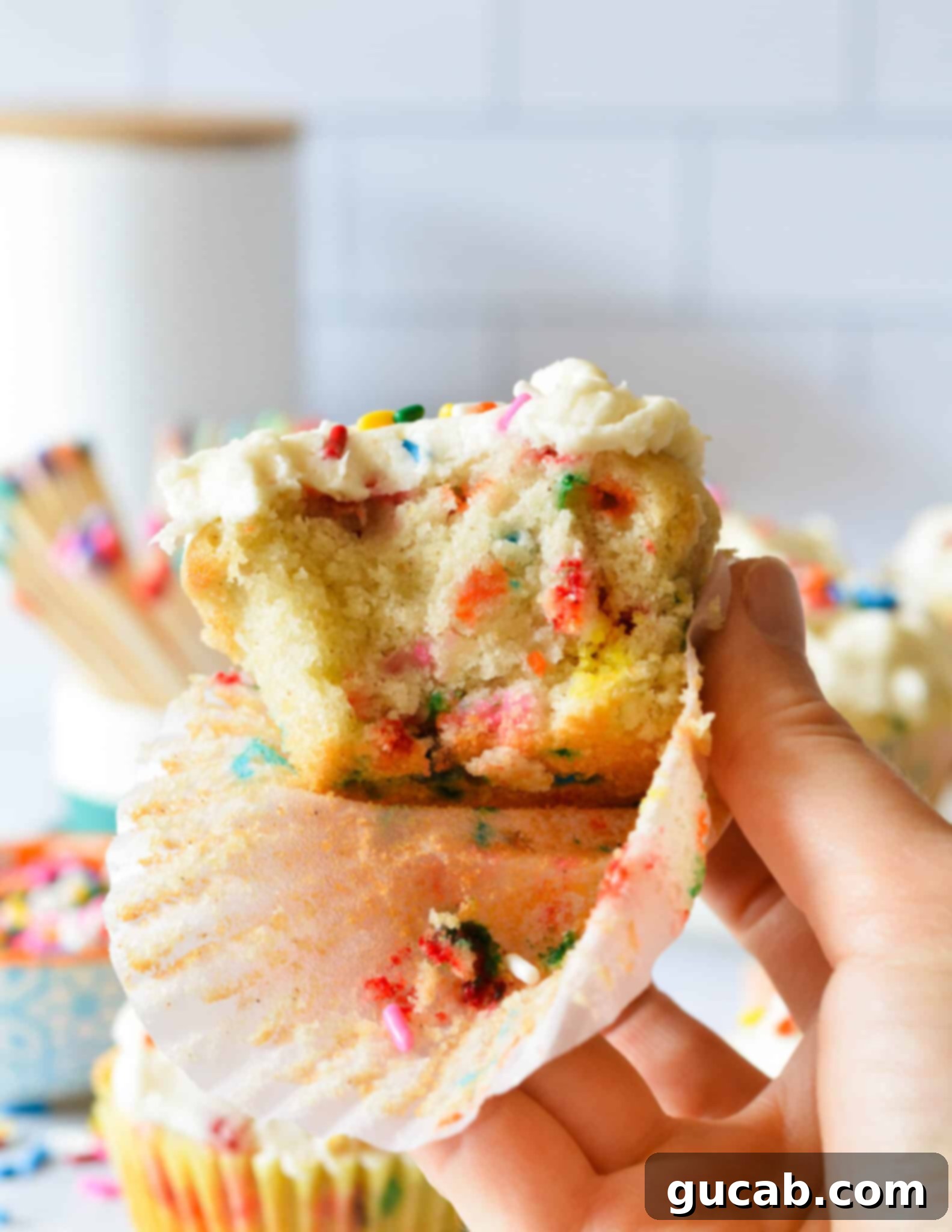 A close-up of a hand holding a gluten-free sprinkle cupcake, highlighting its delicate crumb and colorful jimmies.
