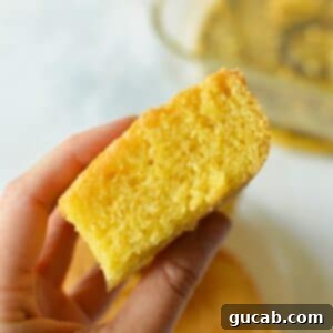 A hand holding a slice of golden almond flour cornbread, ready to be eaten.